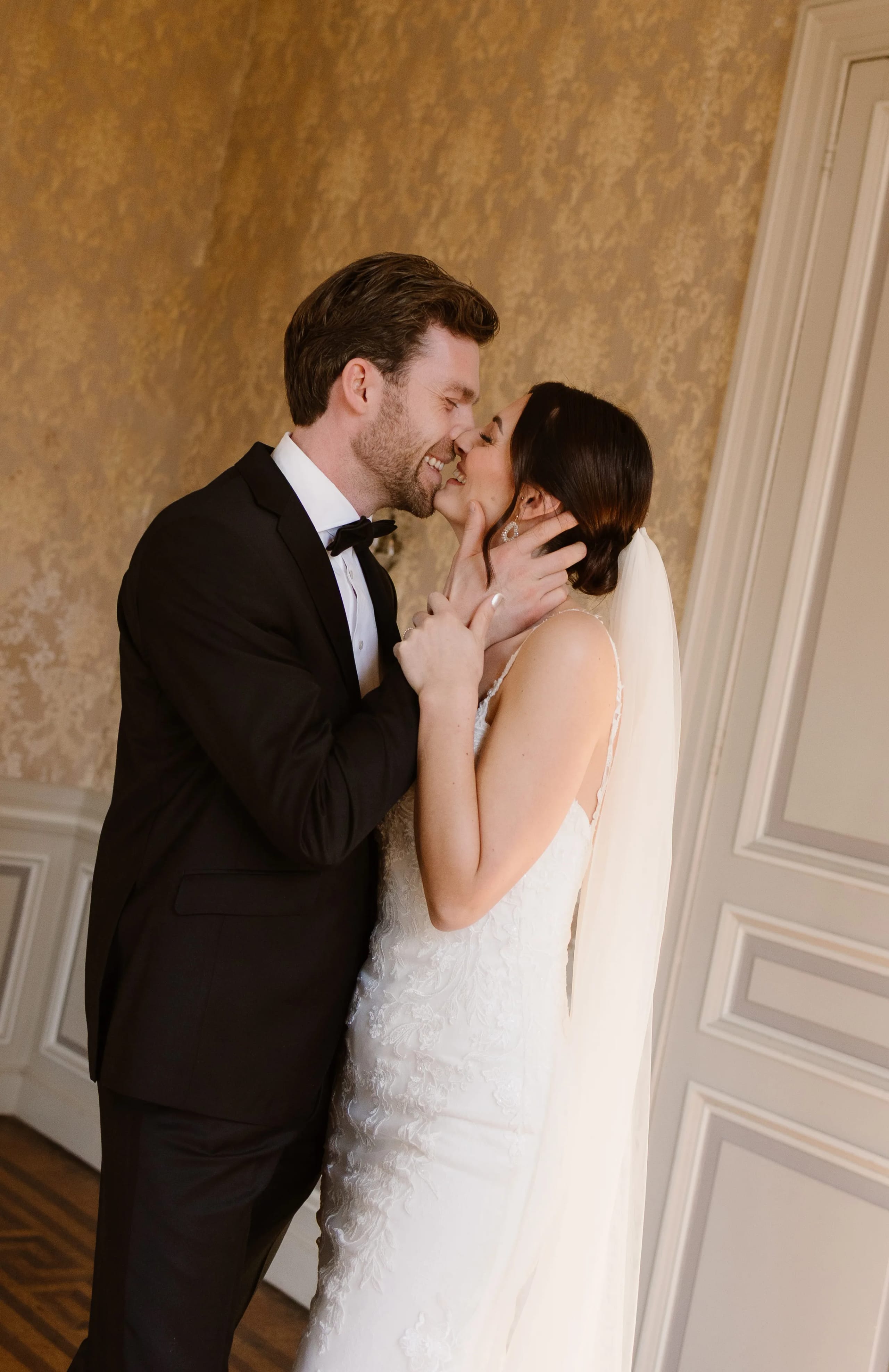 Een verliefd stel, gekleed in formele bruidskleding, kust elkaar intiem in een elegante zaal met een luxe achtergrond, wat een romantische sfeer creëert.