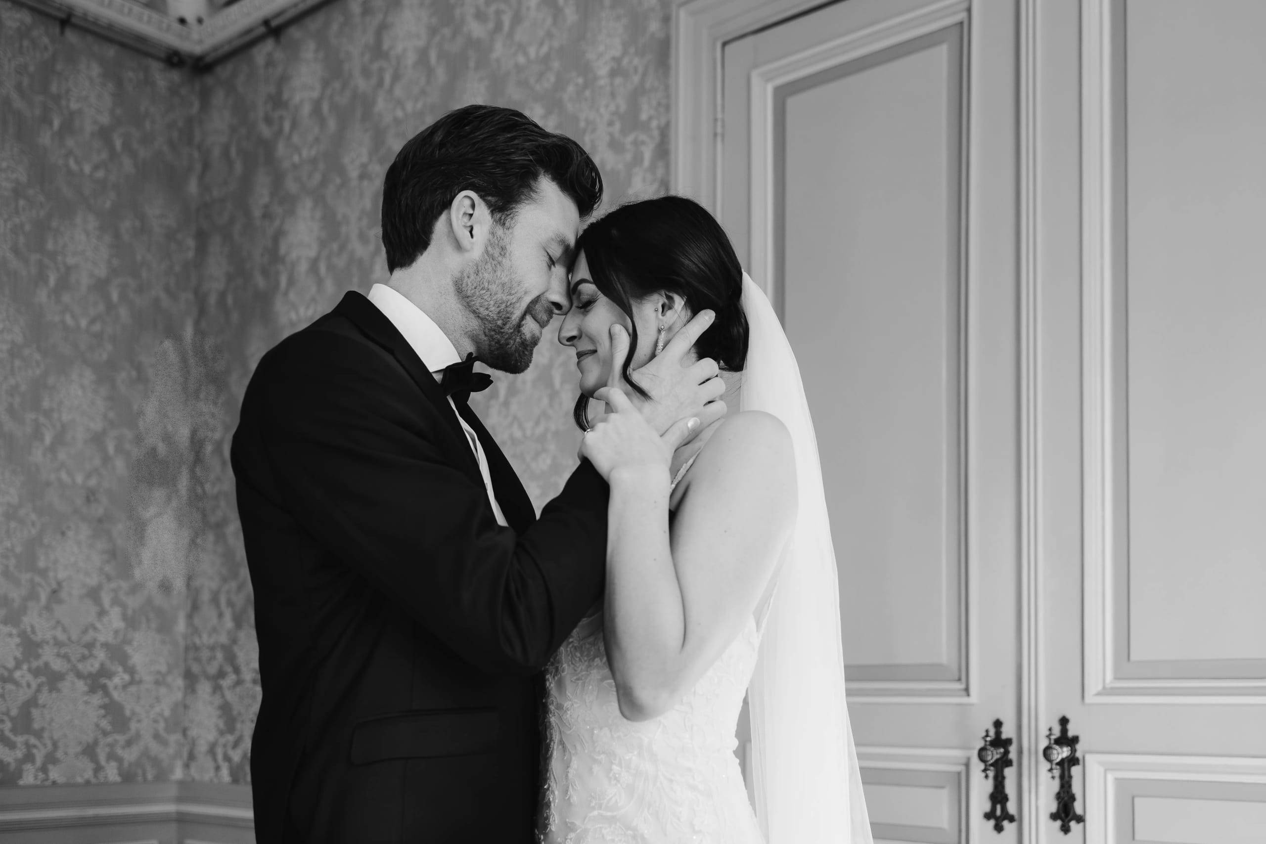 Een gelukkig stel in formele trouwkleding omarmt elkaar intiem in een elegante kamer, met een romantische sfeer die de liefde tussen hen benadrukt.