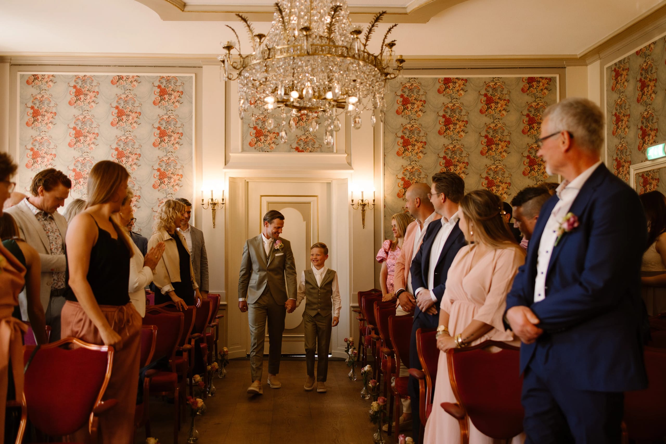 Bruidegom en bruidsjonken lopen door het gangpad in trouwzaal Chateau Marquette