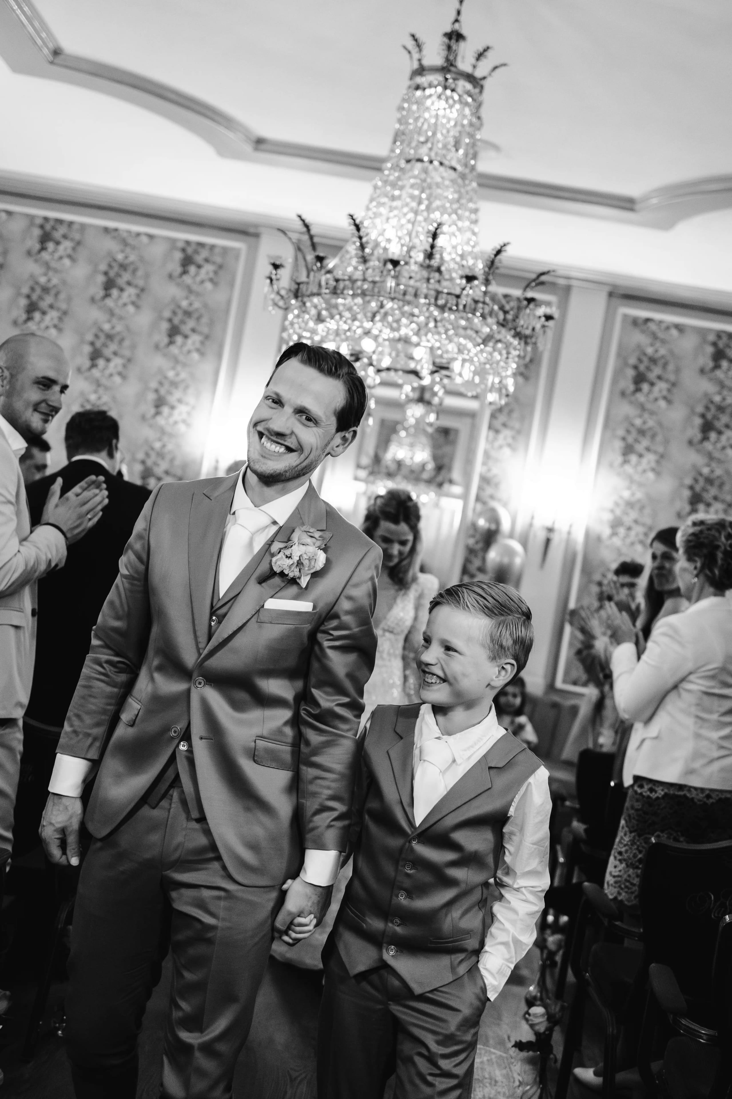 Zwart-wit foto van het dolgelukkige bruidspaar en kind in het gangpad na het ja-woord