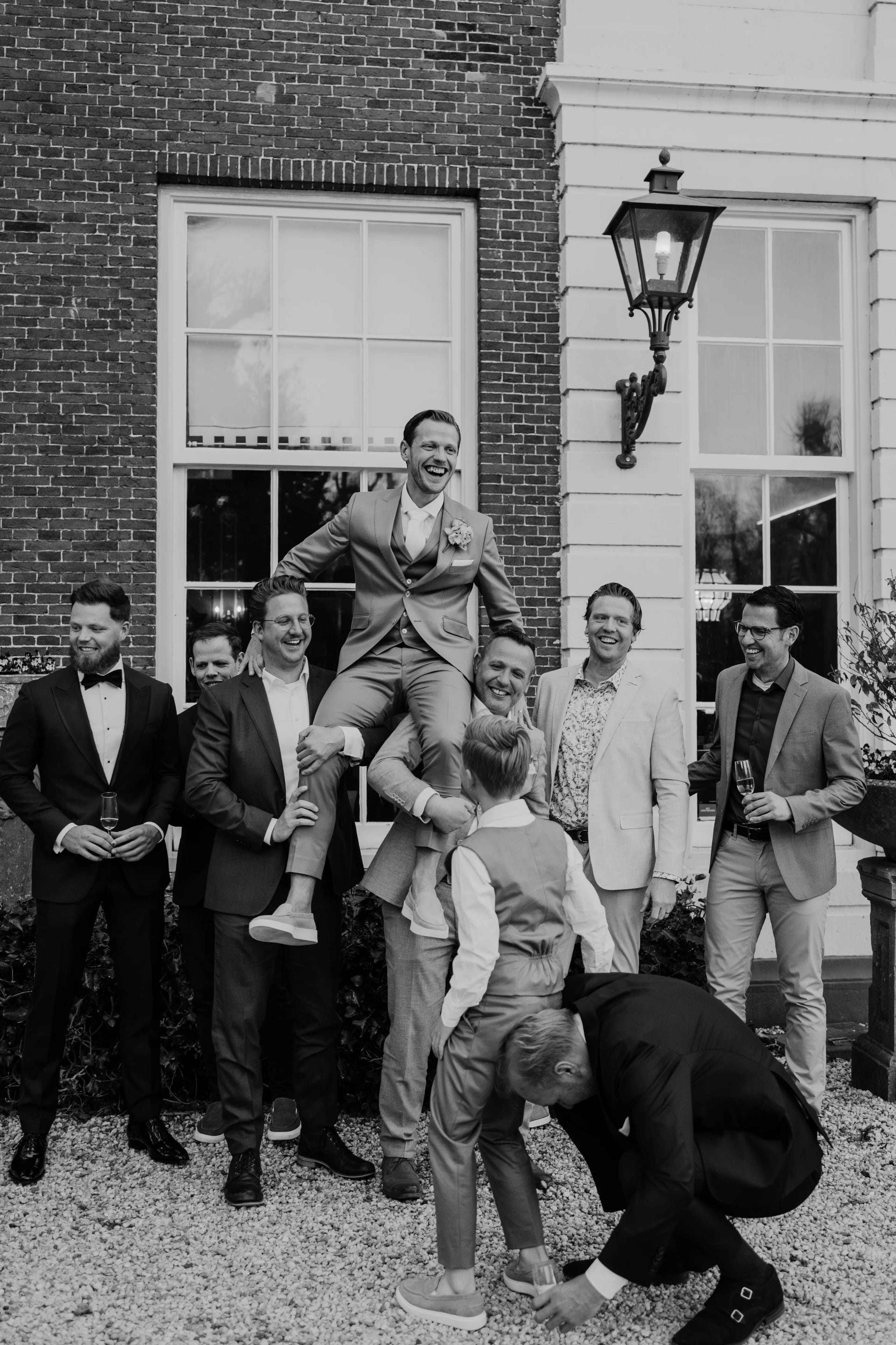 Zwart-wit foto van de lachende bruidegom die door vrienden vrolijk in de lucht wordt getild