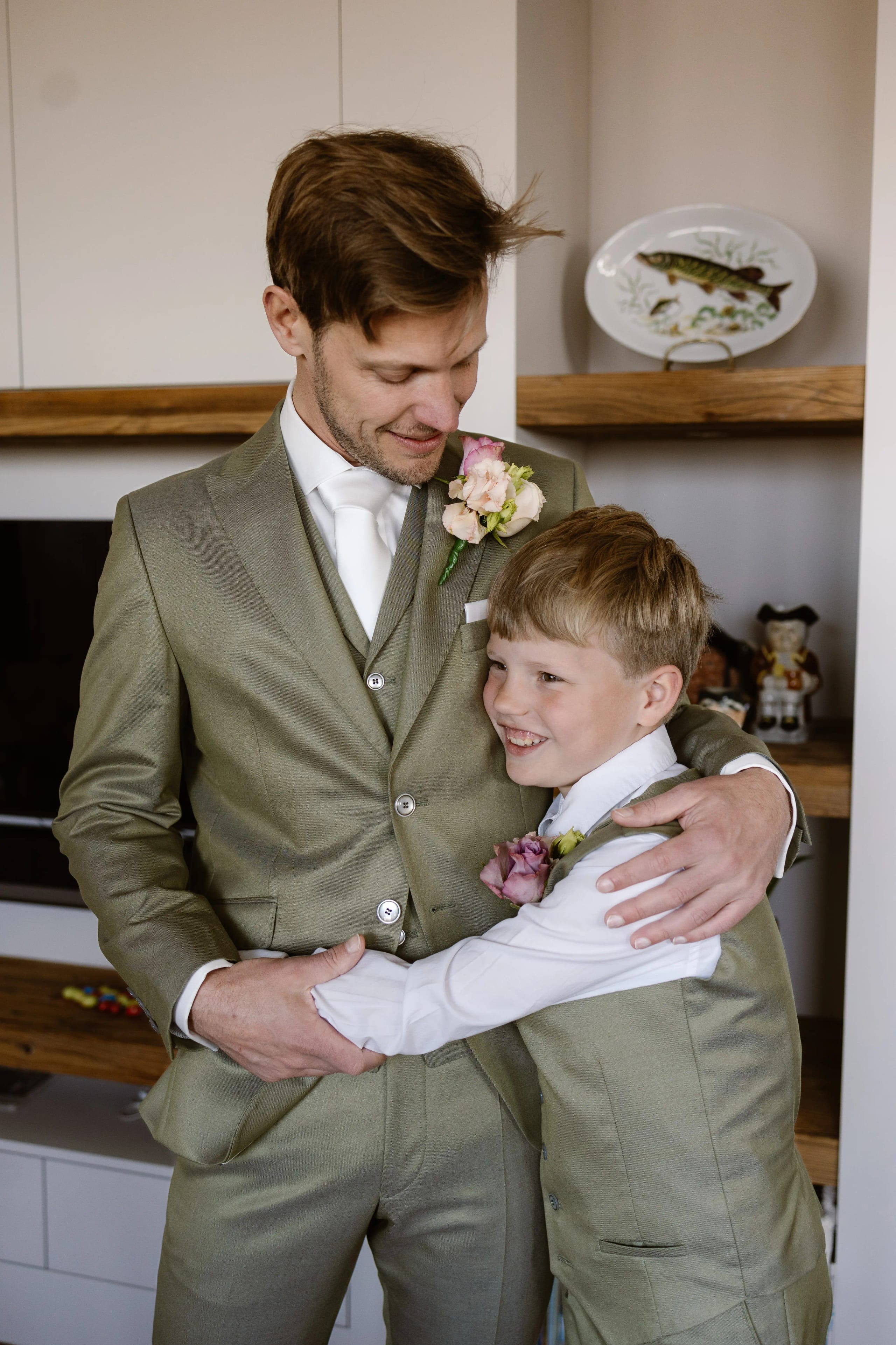 Liefdevolle knuffel tussen de bruidegom en het bruidsjonkertje in matchend groen pak