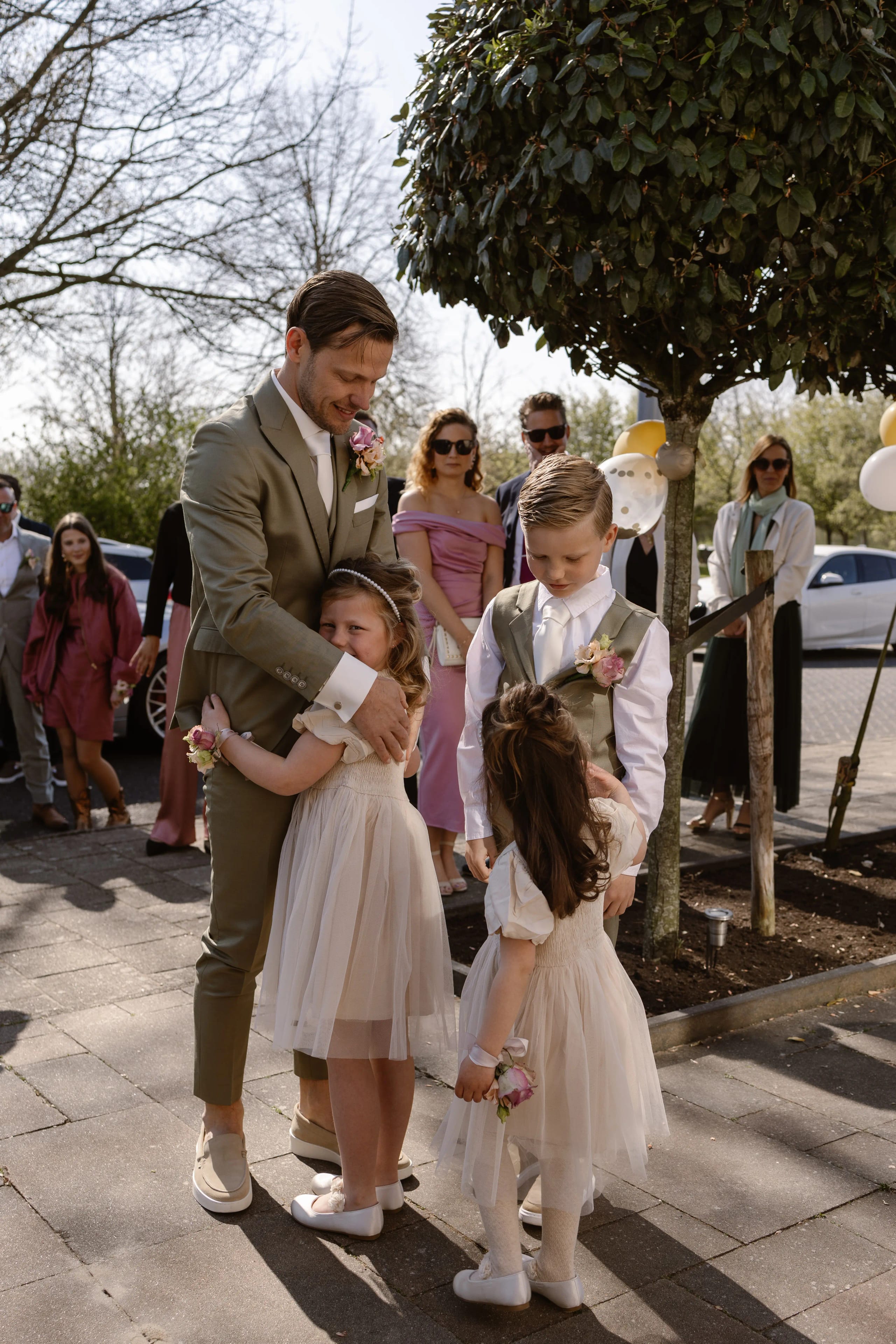 Bruidspaar en bruidskinderen staan ontspannen hand in hand in de buitenlucht