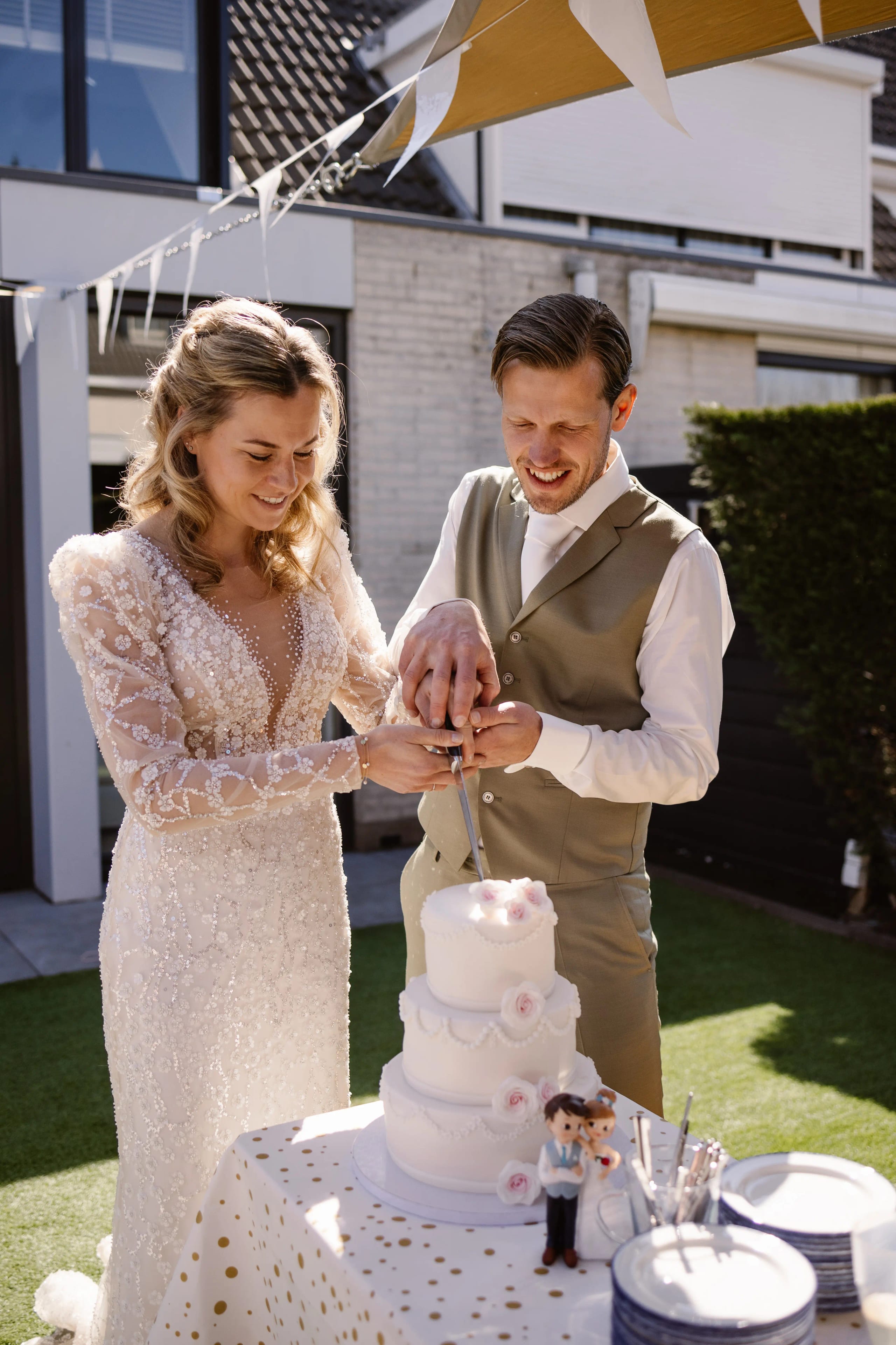 Bruid en bruidegom snijden buiten vrolijk samen hun witte bruidstaart aan