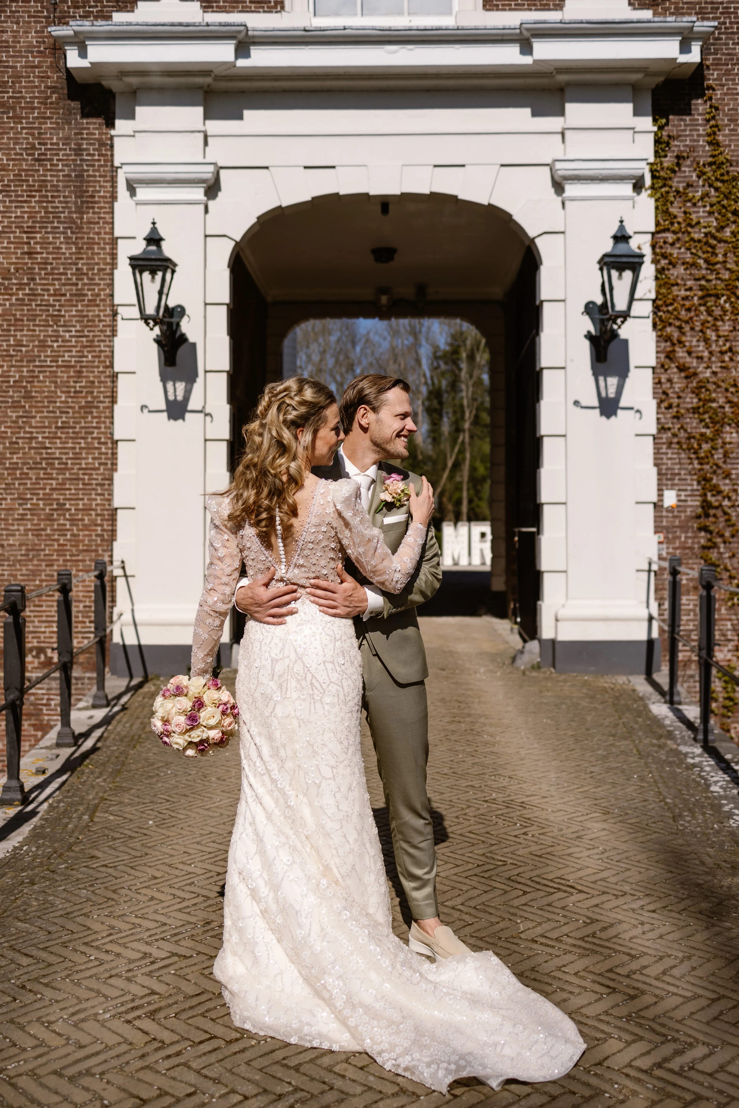 Bruidspaar kijkt elkaar liefdevol aan in de zonnige binnenplaats op het kasteellandgoed