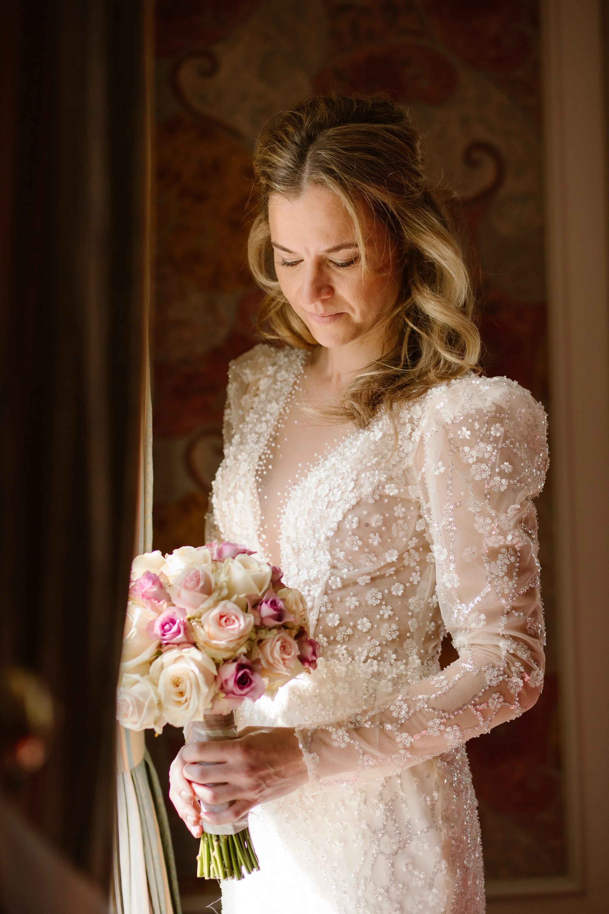 De bruid bewondert haar roze een crèmekleurige bruidsboeket in sfeervol licht