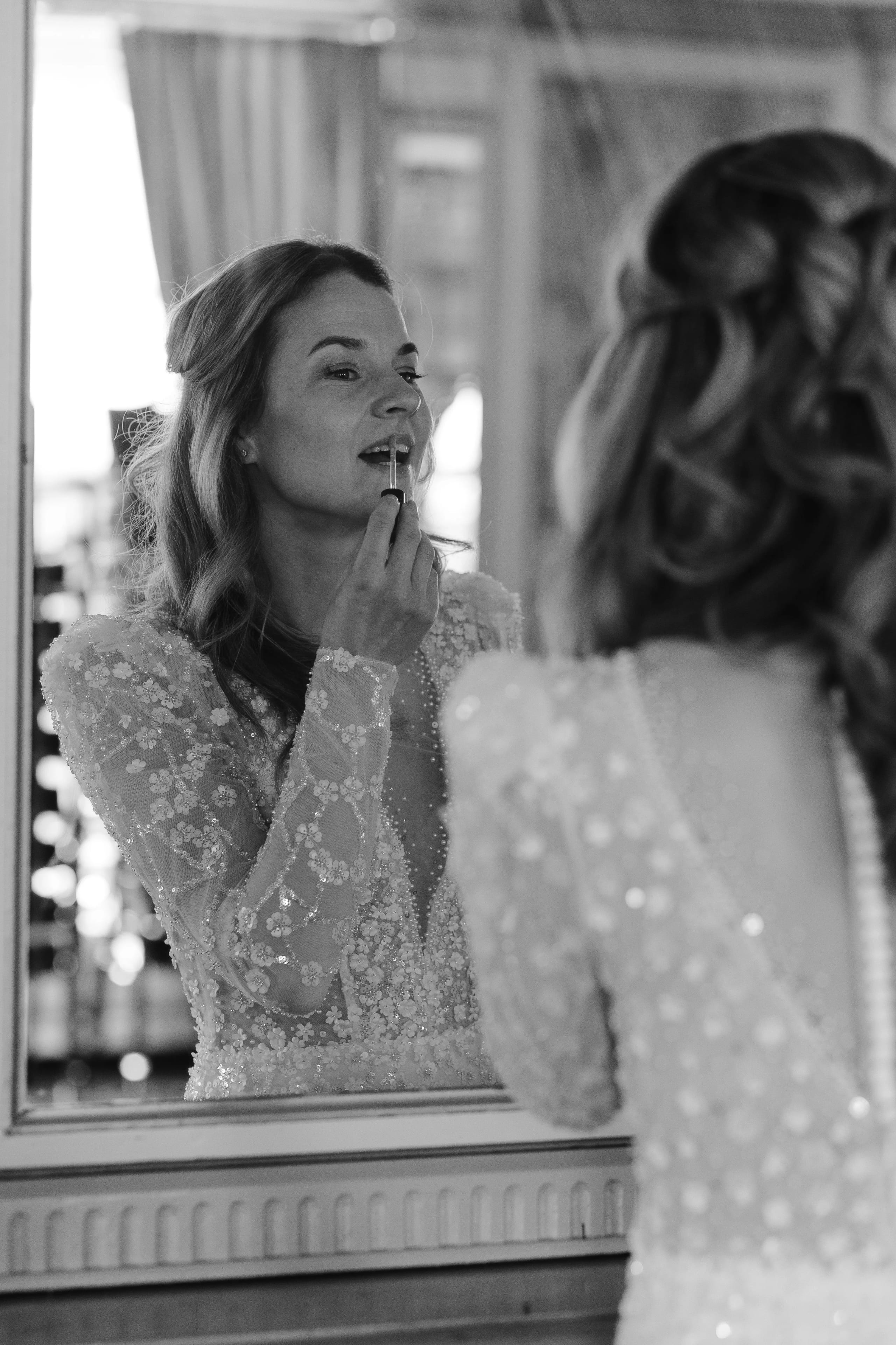 Zwart-wit reflectie van de bruid in de spiegel die haar lippenstift bijwerkt