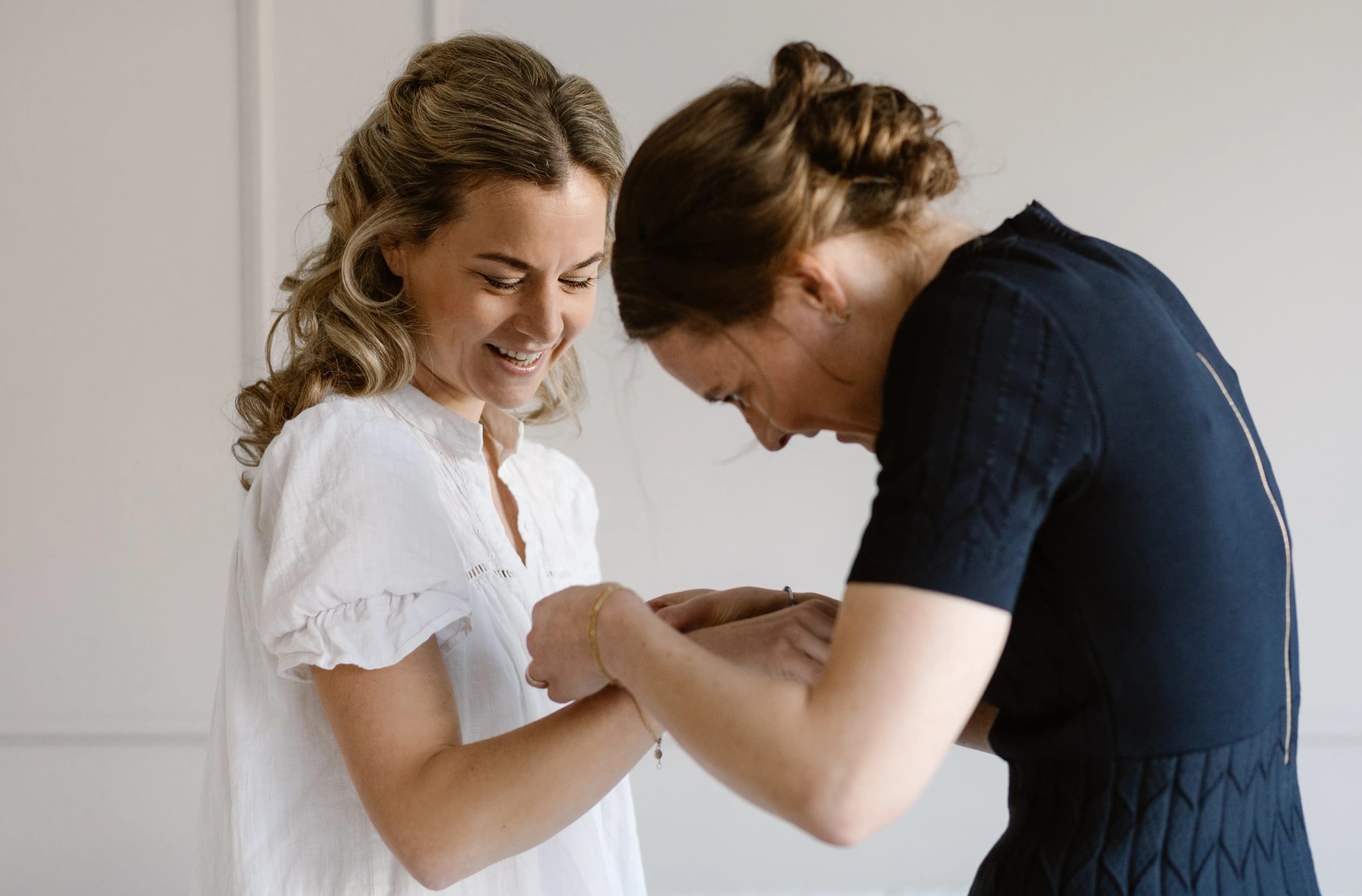 Lachende bruid helpt een gast met een armbandje tijdens de ochtendvoorbereidingen