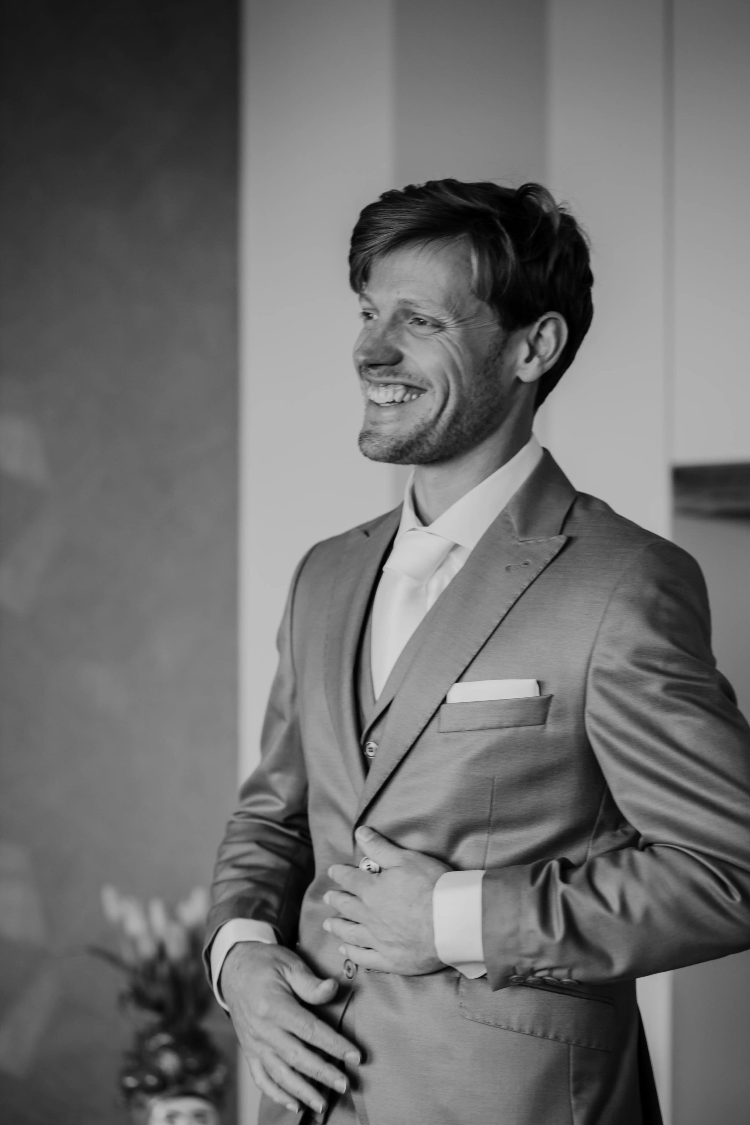 Zwart-wit portret van de knappe en lachende bruidegom in zijn trouwpak