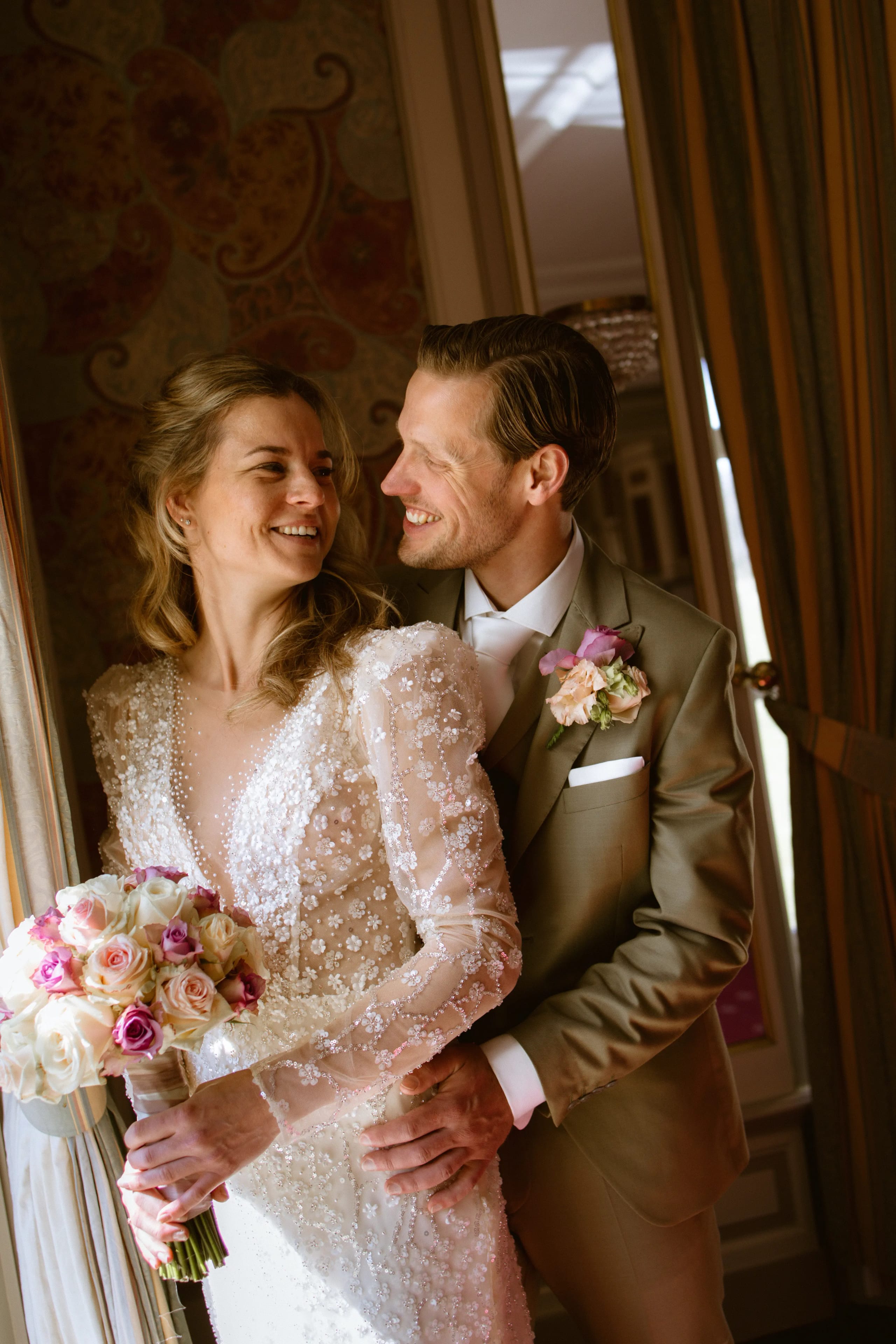 Intiem portret van de lachende bruid en bruidegom die teder knuffelen binnenshuis