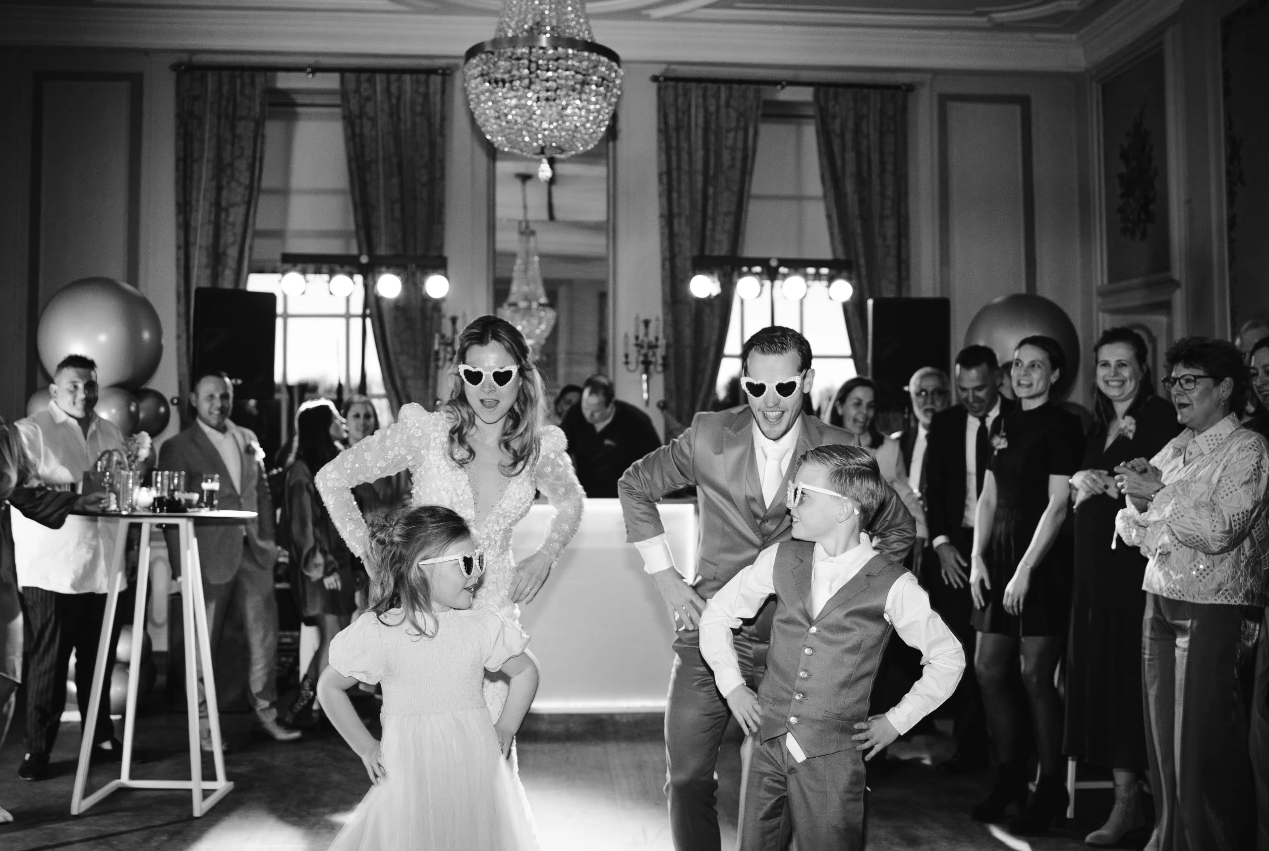 Zwart-wit foto van het dolgelukkige bruidspaar en een kind feestend met hartjeszonnebrillen op