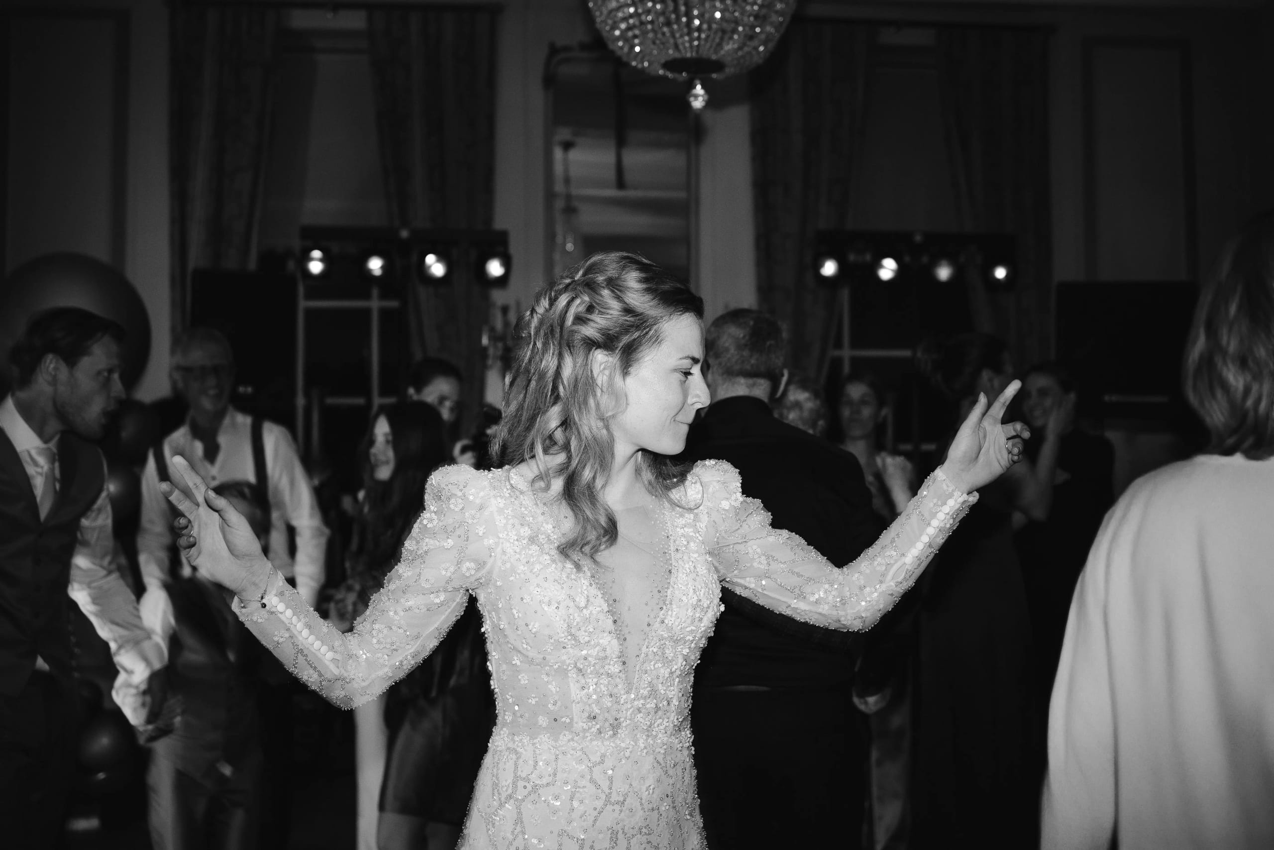 Zwart-wit sfeerfoto van de uitzinnige bruid in haar fonkeljurk dansend met haar armen in de lucht