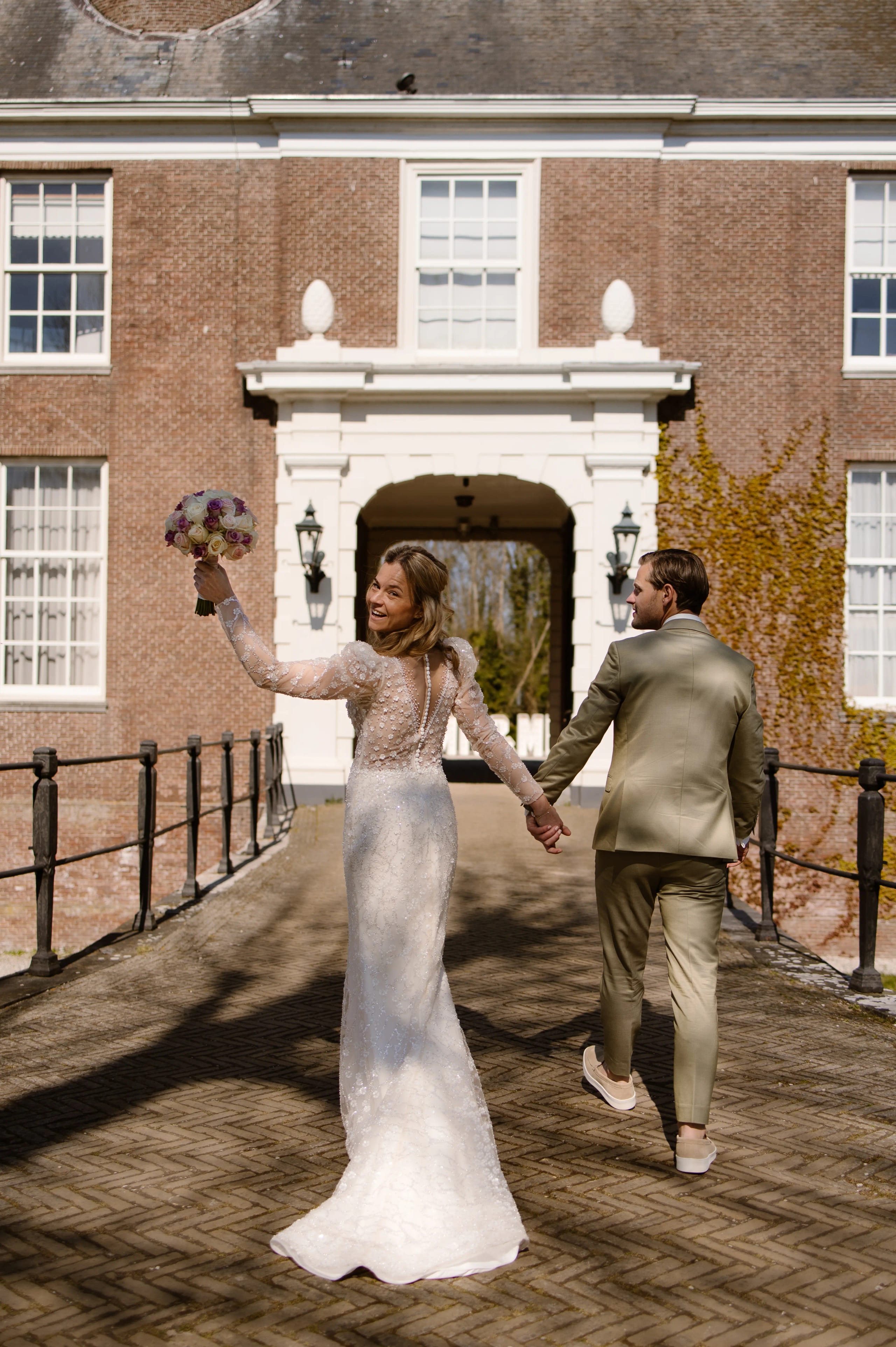 Pasgetrouwd bruidspaar loopt hand in hand de brug over met het bruidsboeket in de lucht