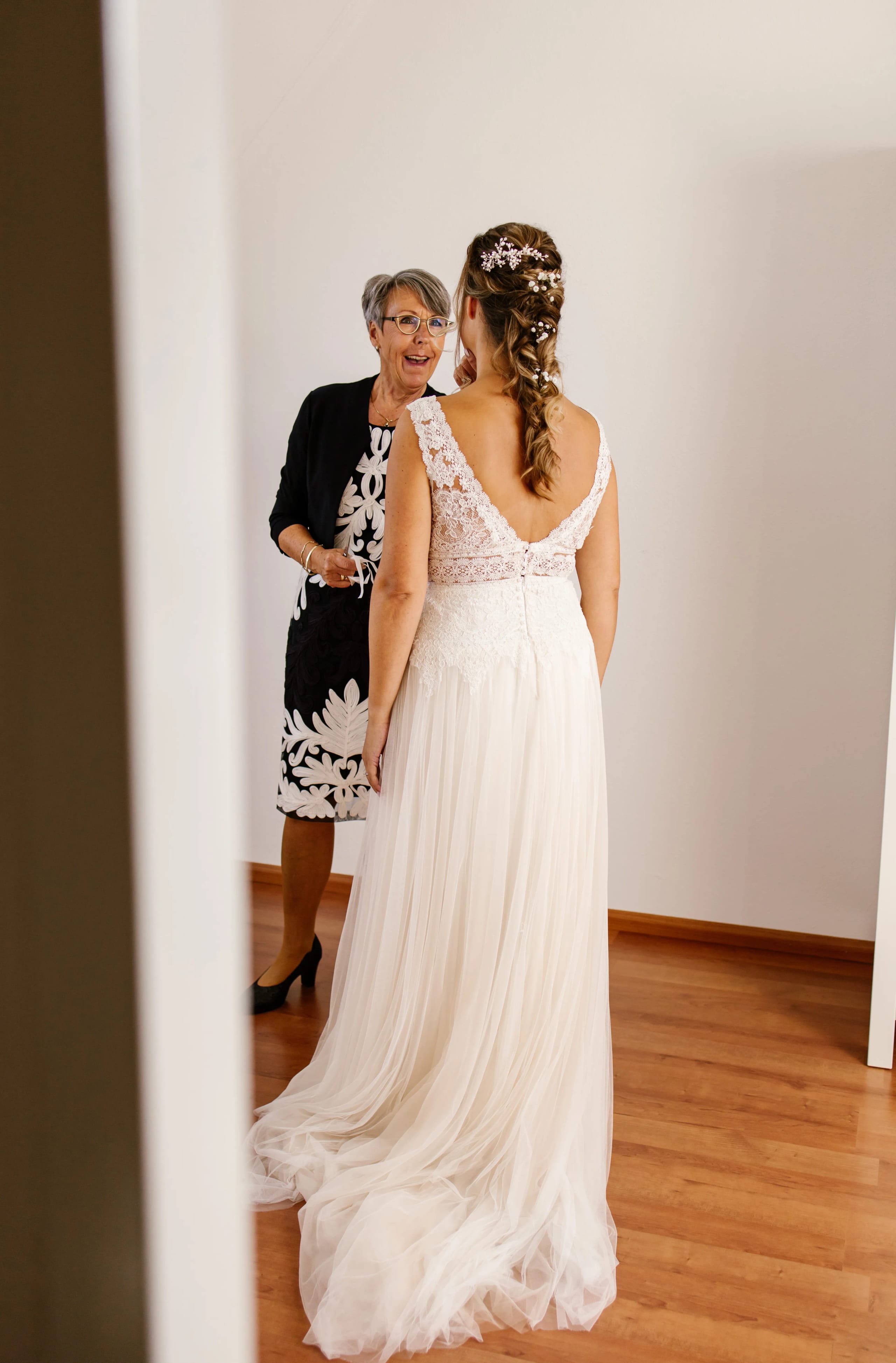 De bruid in haar prachtige kanten trouwjurk wordt geholpen door een guest die haar jurk strikt