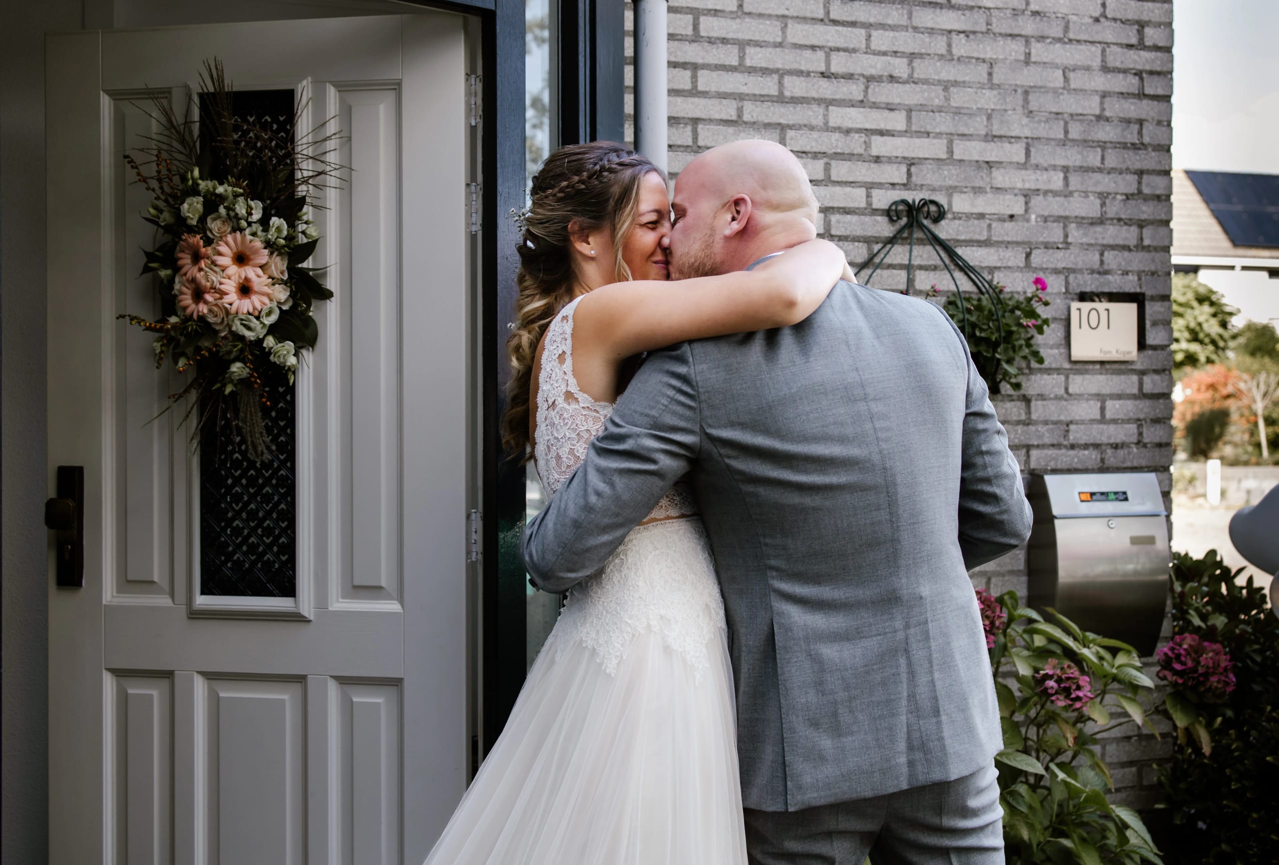 Bruidspaar deelt een romantische eerste kus bij de voordeur van hun woning
