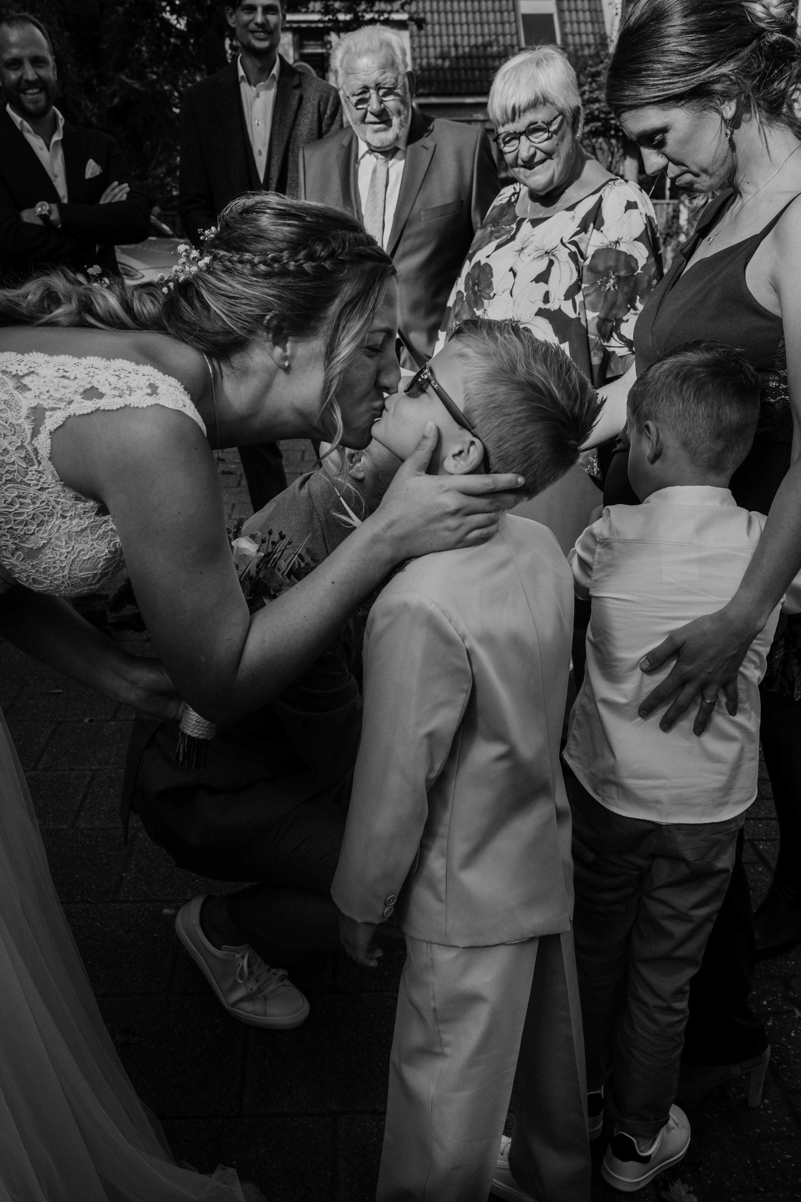 Sfeervol zwart-wit beeld van de bruid die een kind een kus op de wang geeft