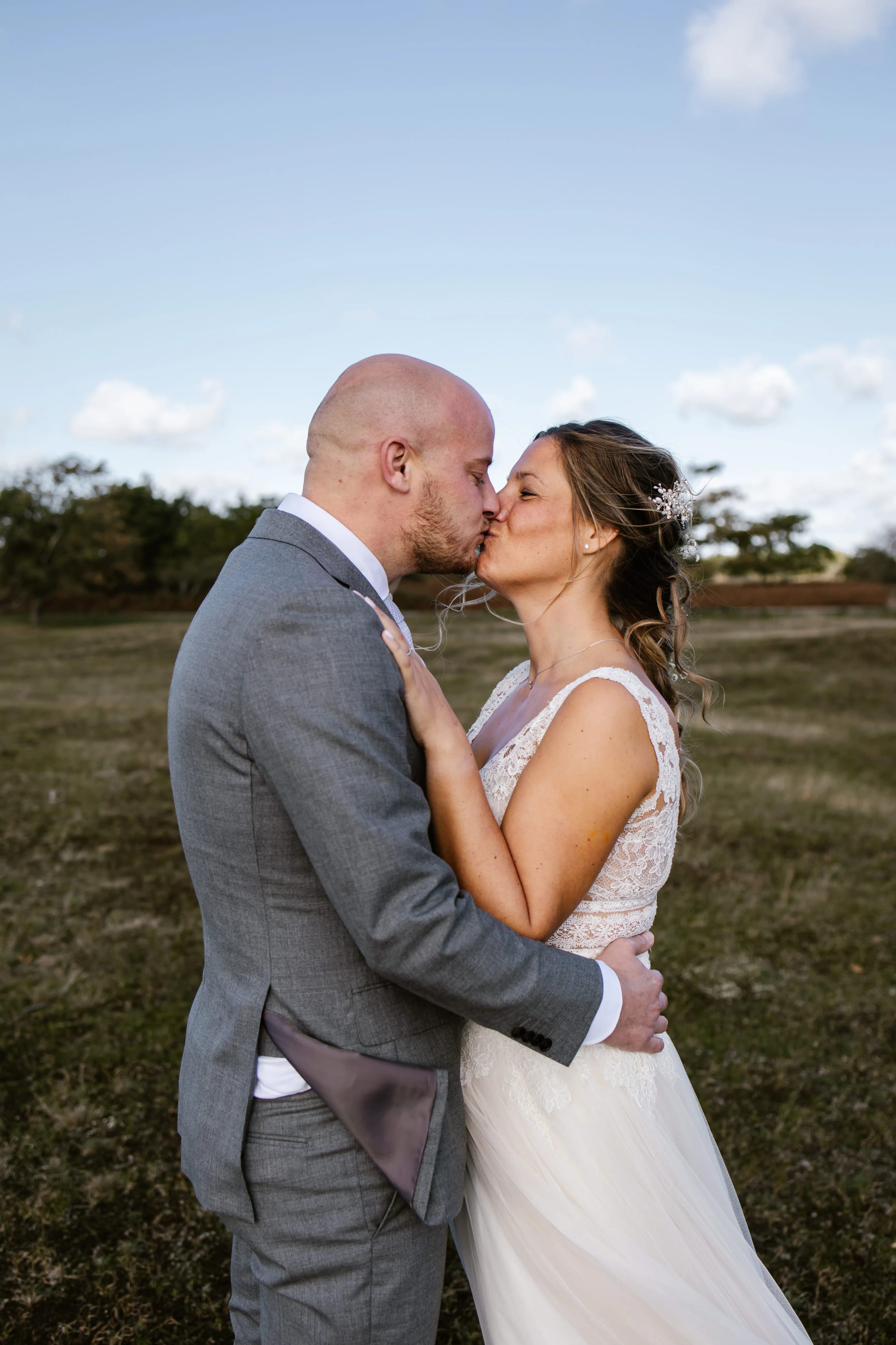 Intieme kus tussen bruid Denise en bruidegom Hein in een zonnig landschap