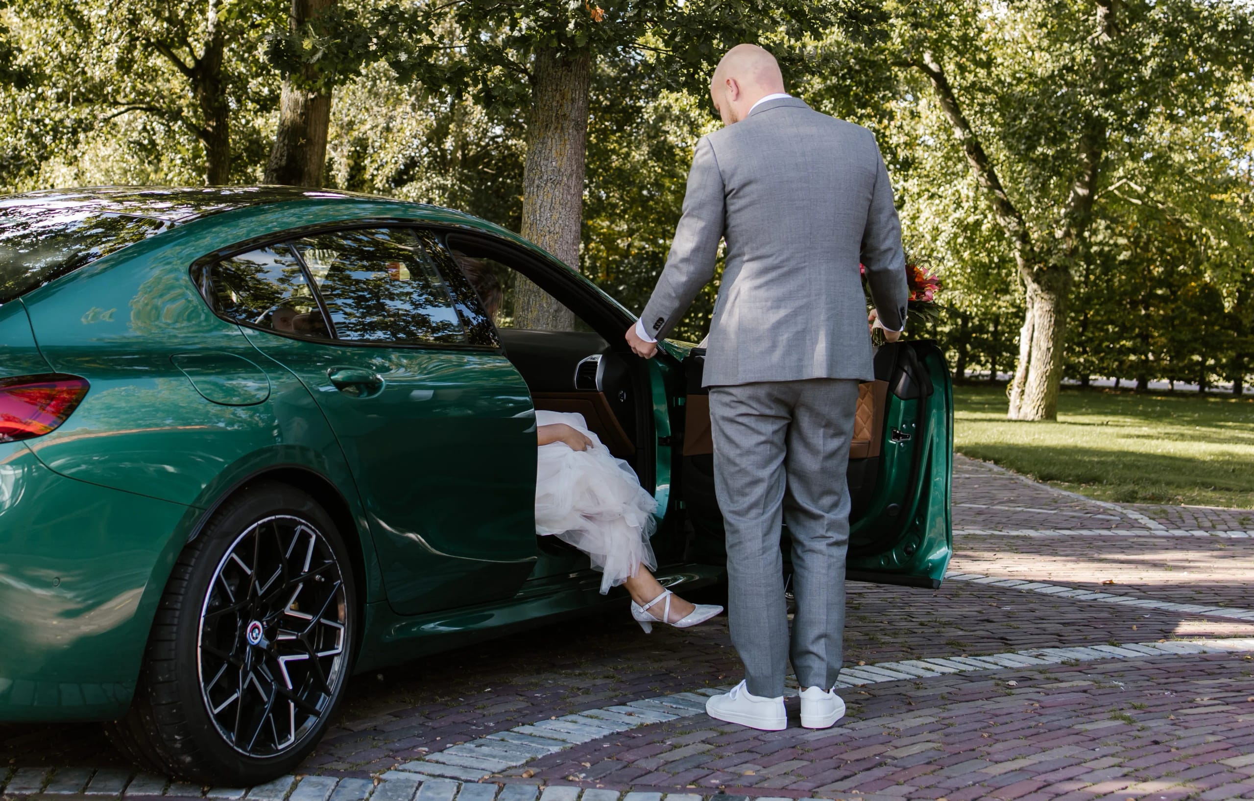 Bruidegom Hein opent de deur van de groene trouwauto voor zijn bruid Denise