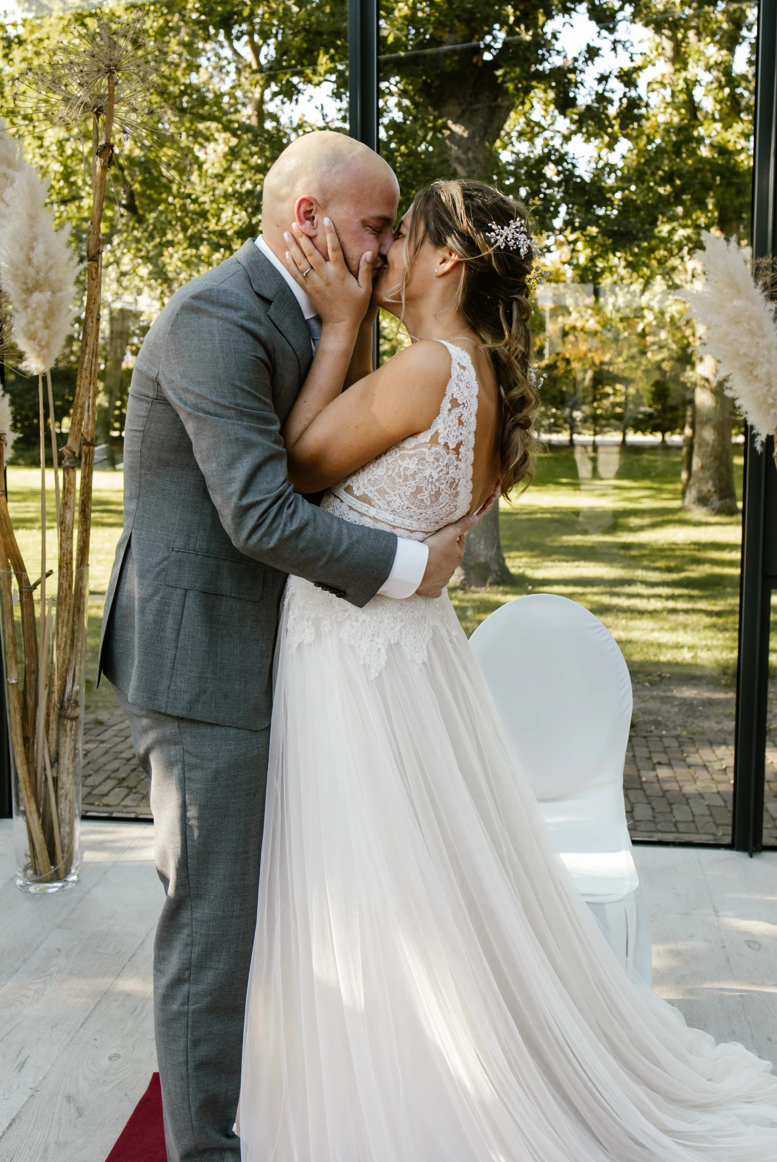 Romantische kus van het bruidspaar voor een glazen wand met uitzicht op bomen