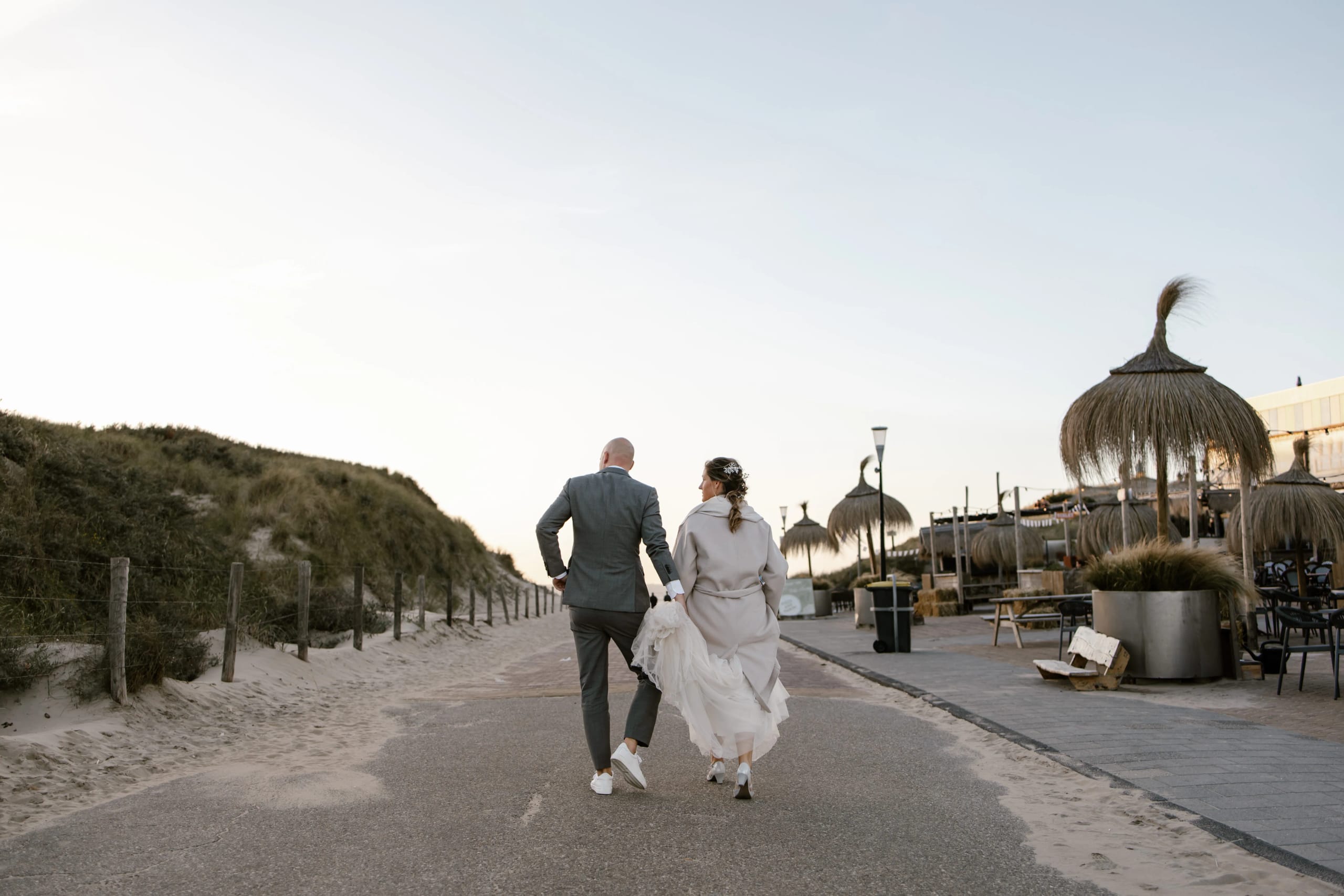 Het bruidspaar wandelt samen over een pad richting het strand bij zonsondergang