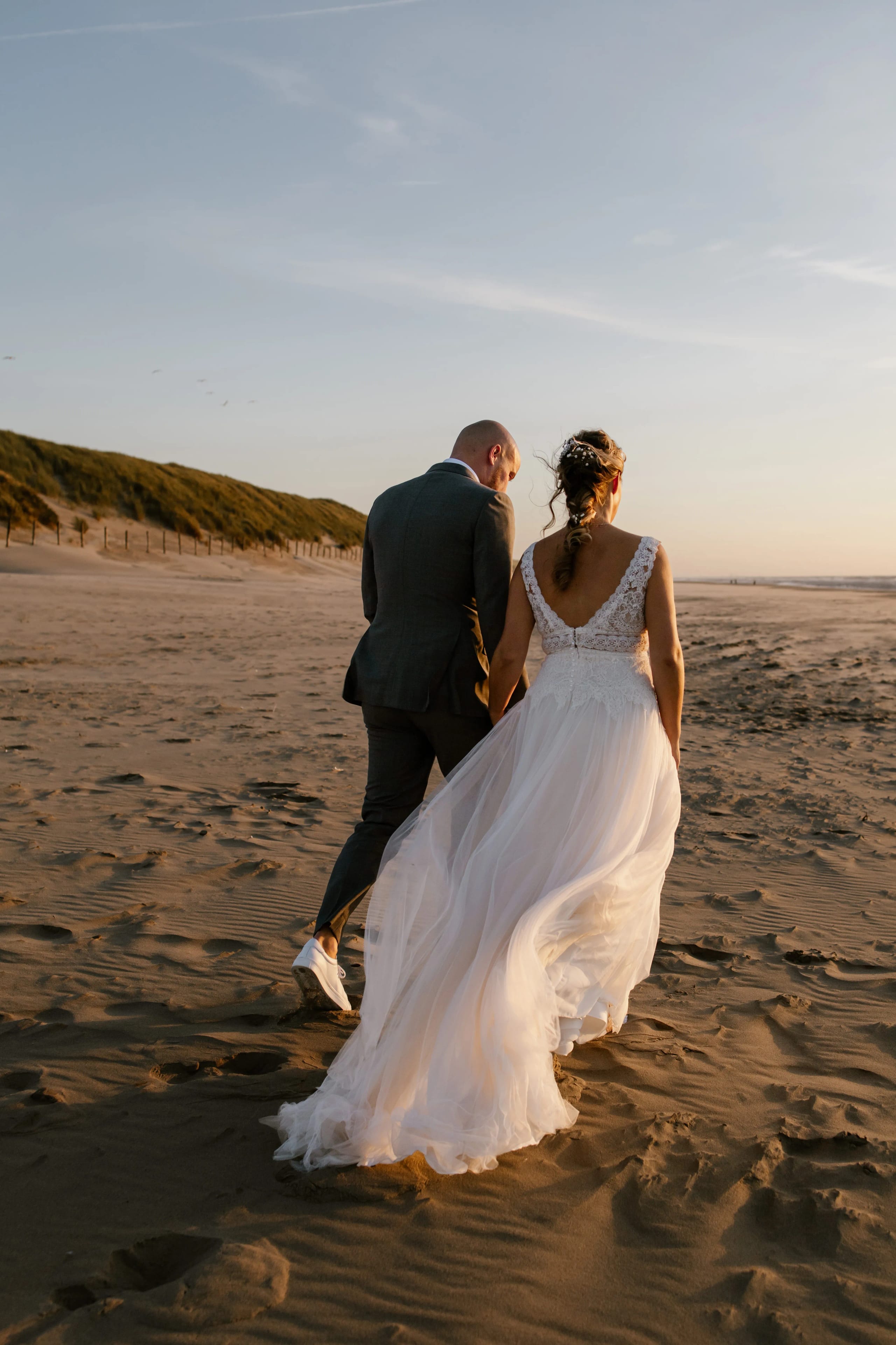 Romantische wandeling van het bruidspaar over het strand terwijl de zon langzaam zakt