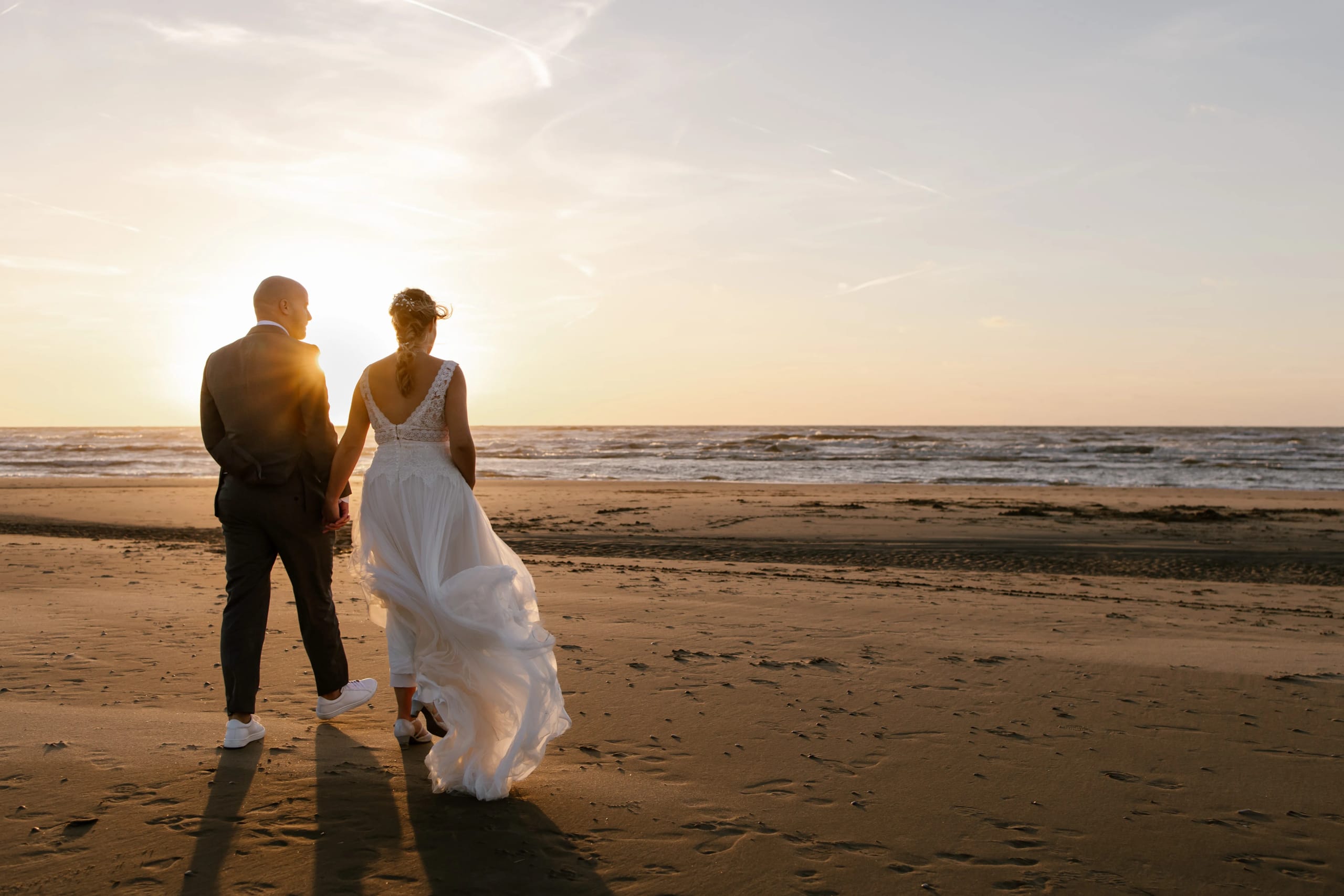 Denise wandelt over het strand terwijl haar witte trouwjurk wappert in de wind