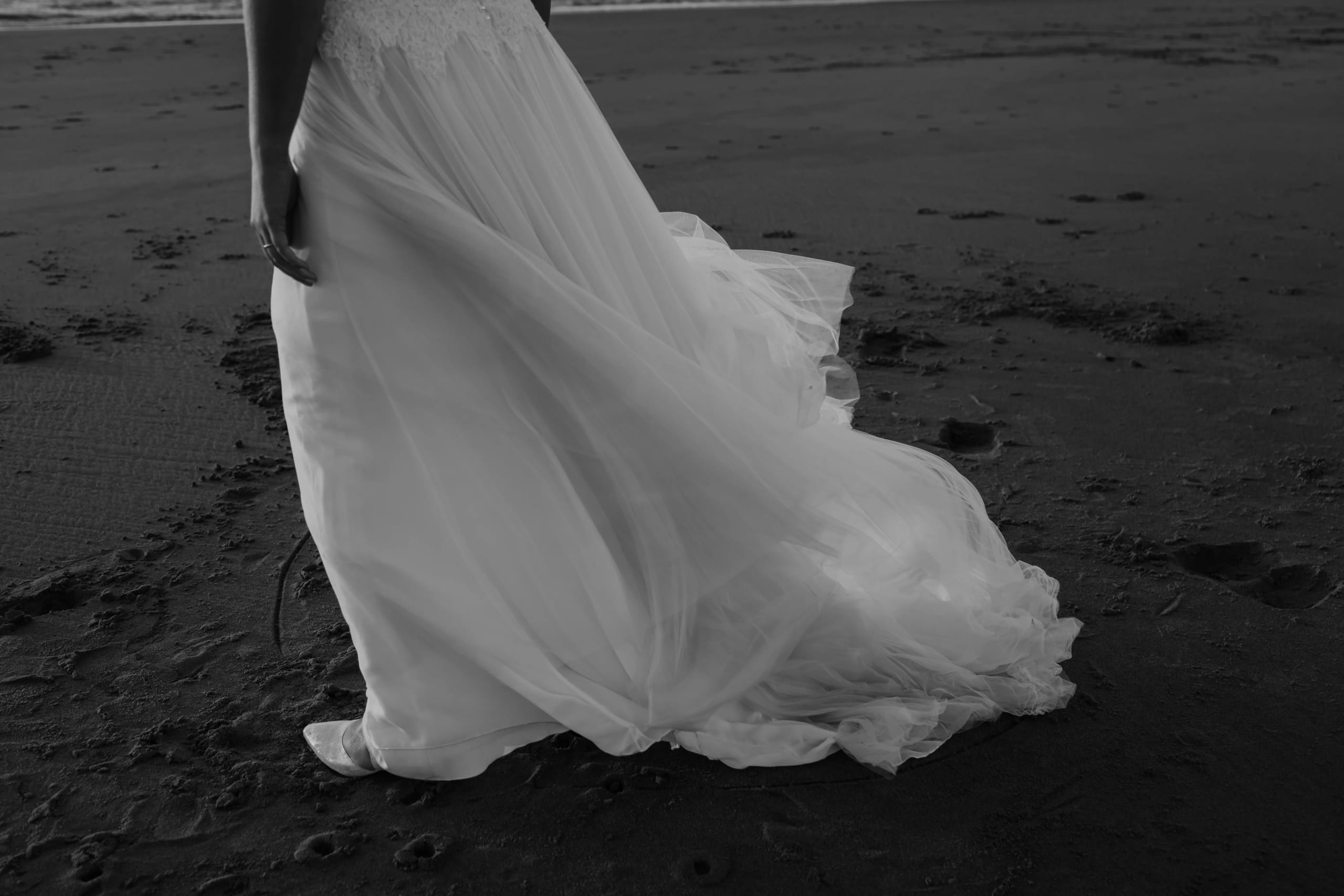 Portret van de stralende bruid Denise die over haar schouder naar de camera kijkt op het strand