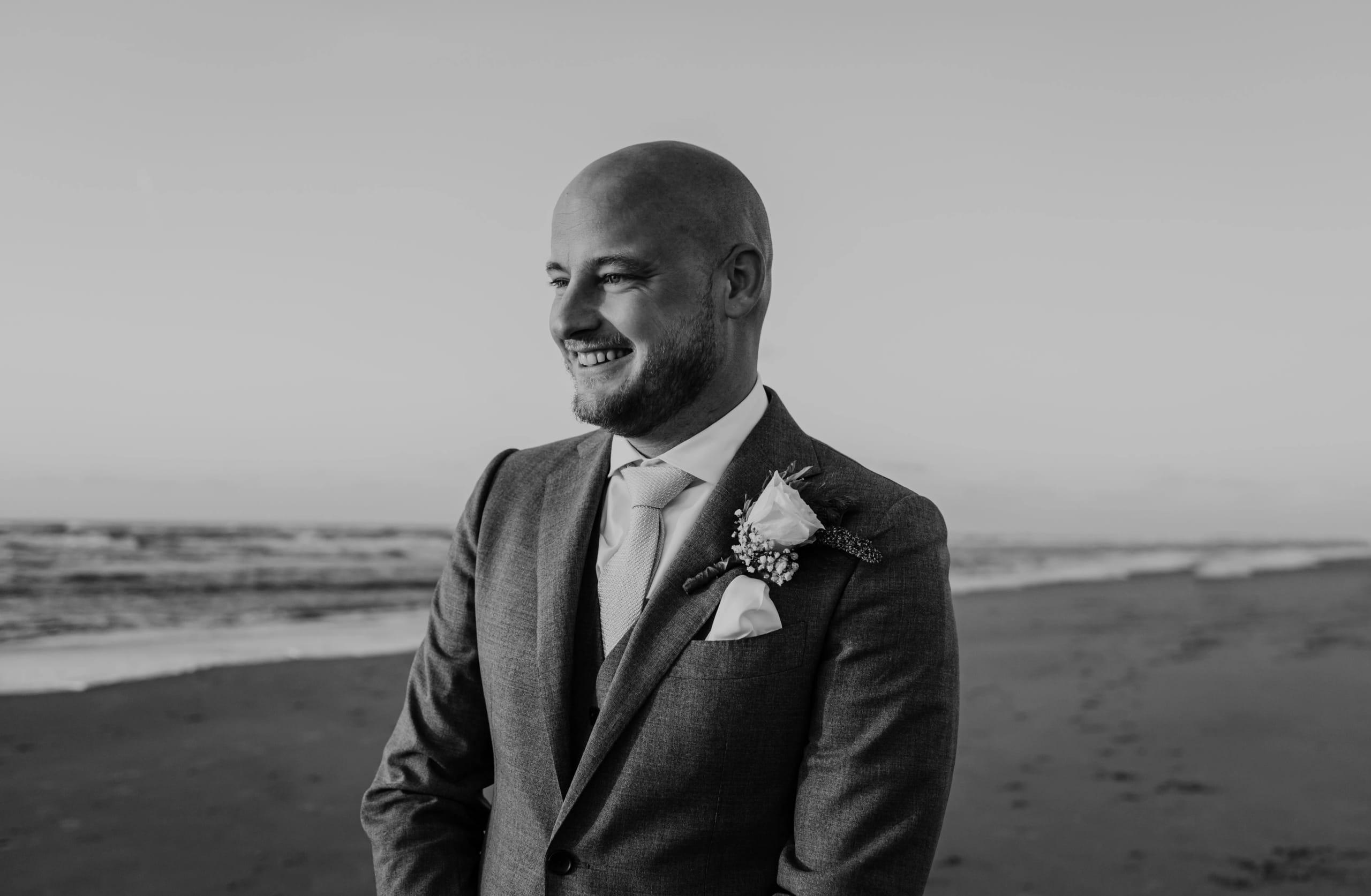 Het bruidspaar staat dicht bij elkaar op het strand in het warme avondlicht