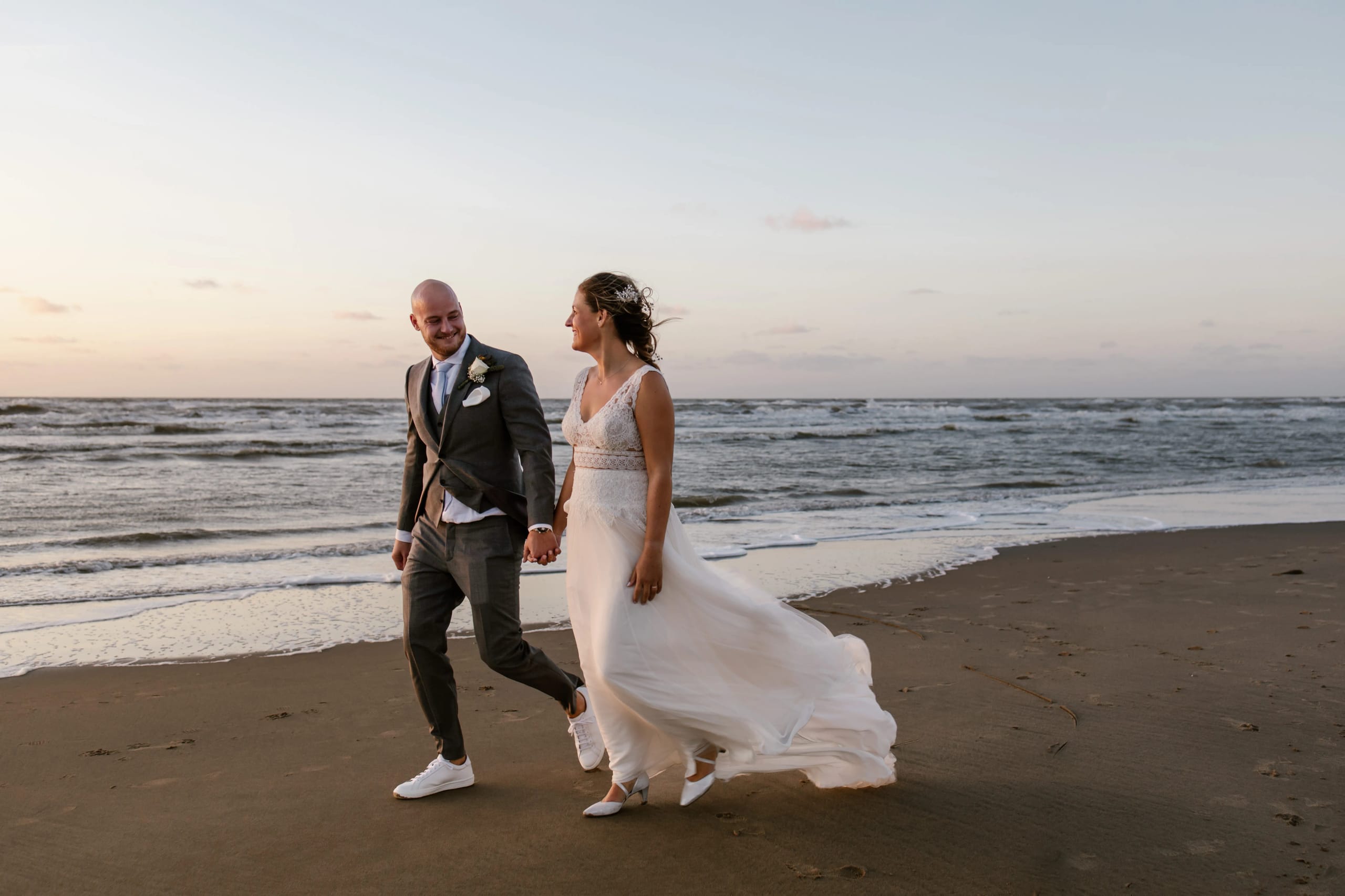 Zwart-wit shot of the rug of the bruid wandelt met de bruidegom langs de vloedlijn