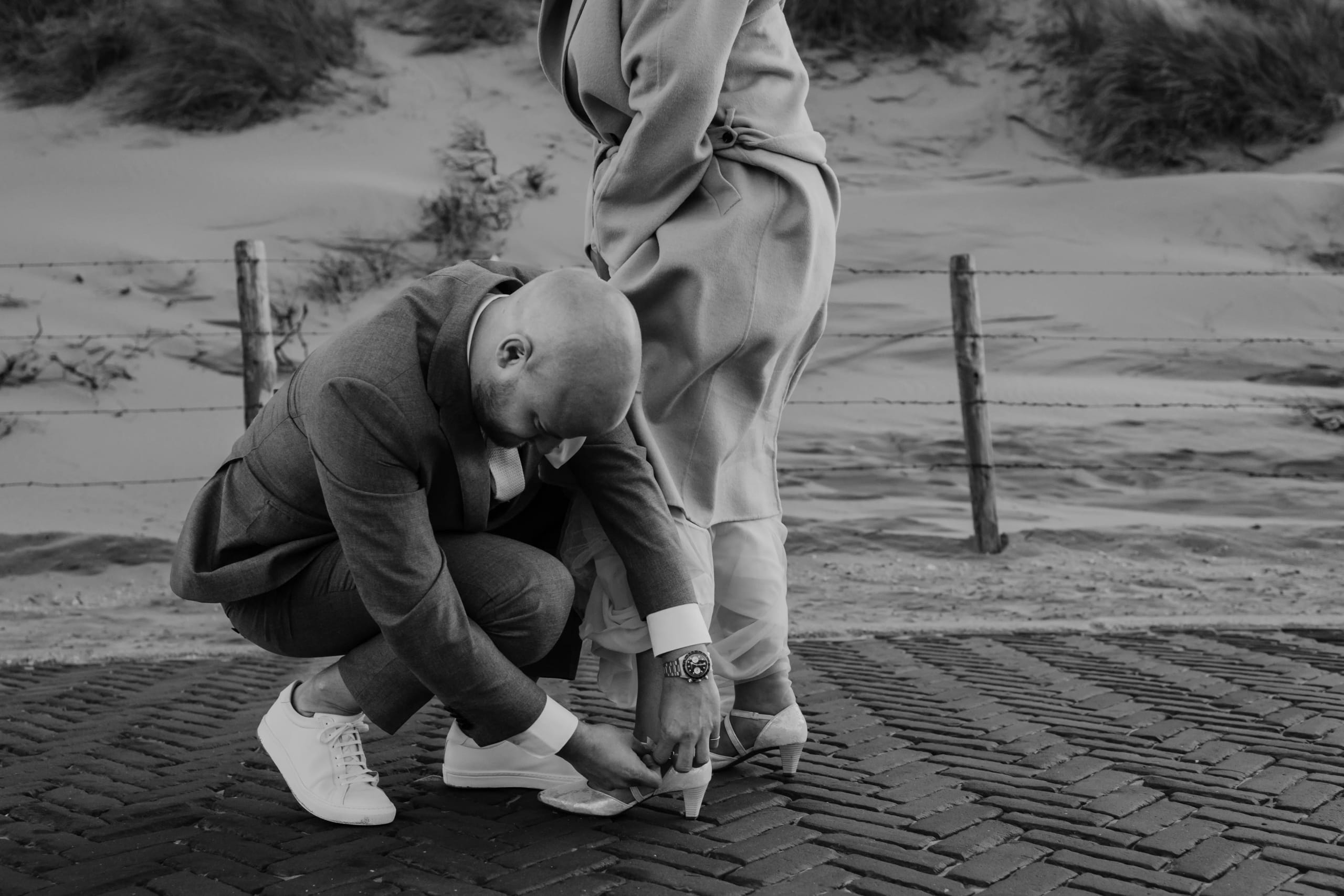 Zwart-wit actieshot of Hein die de schoen of Denise helpt vastmaken op de boulevard