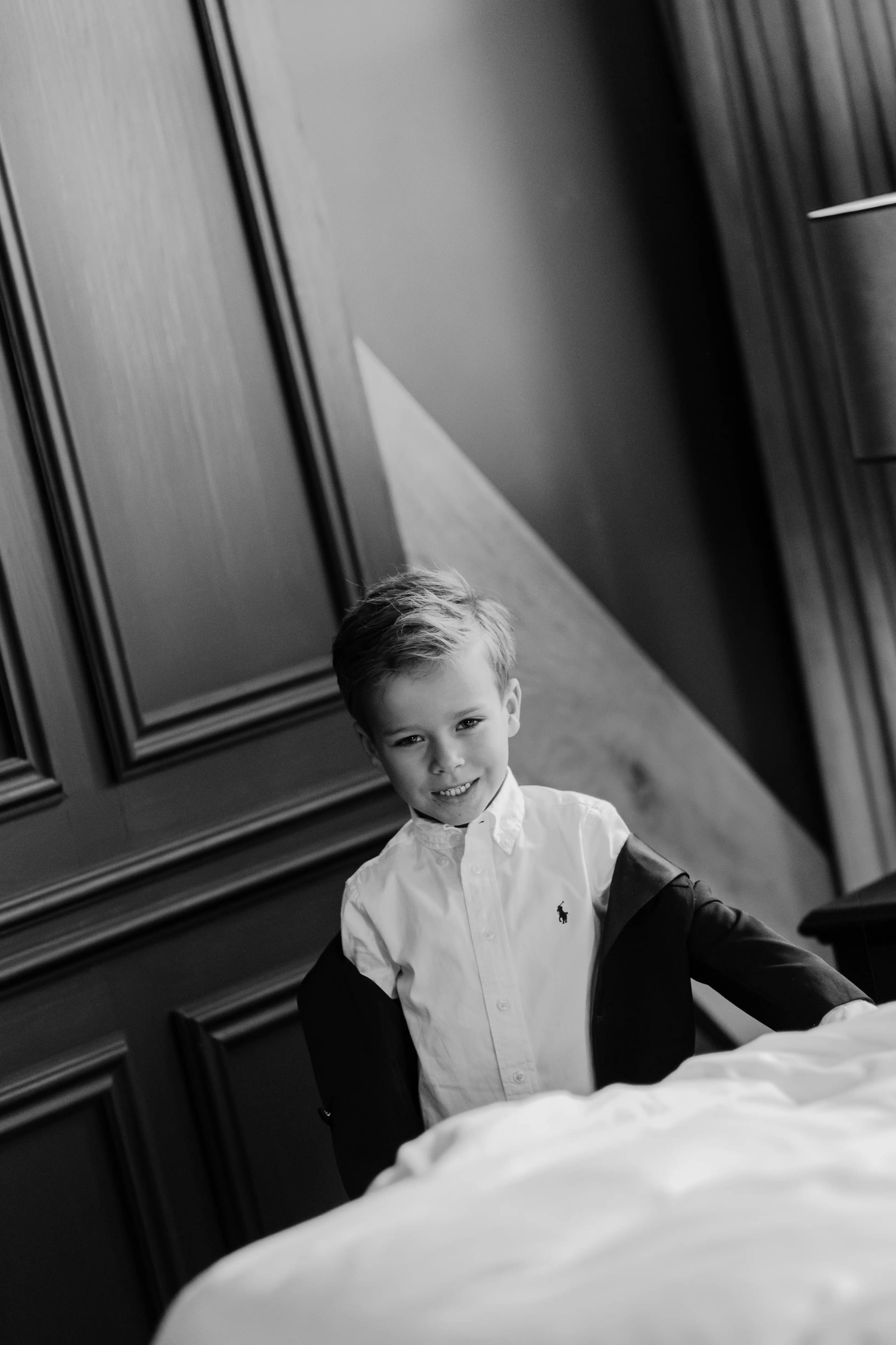 Portret van een lachend kind in een wit overhemd tegen een donkere houten wand