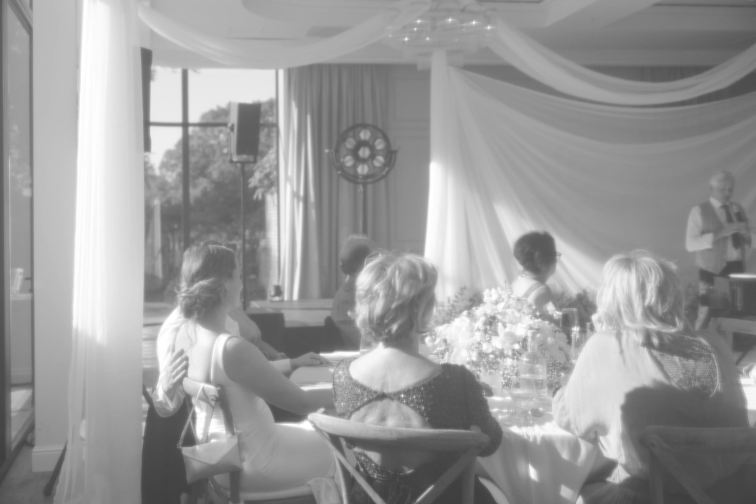 Zwart-wit sfeerbeeld van gasten die dineren in een elegant gedecoreerde zaal