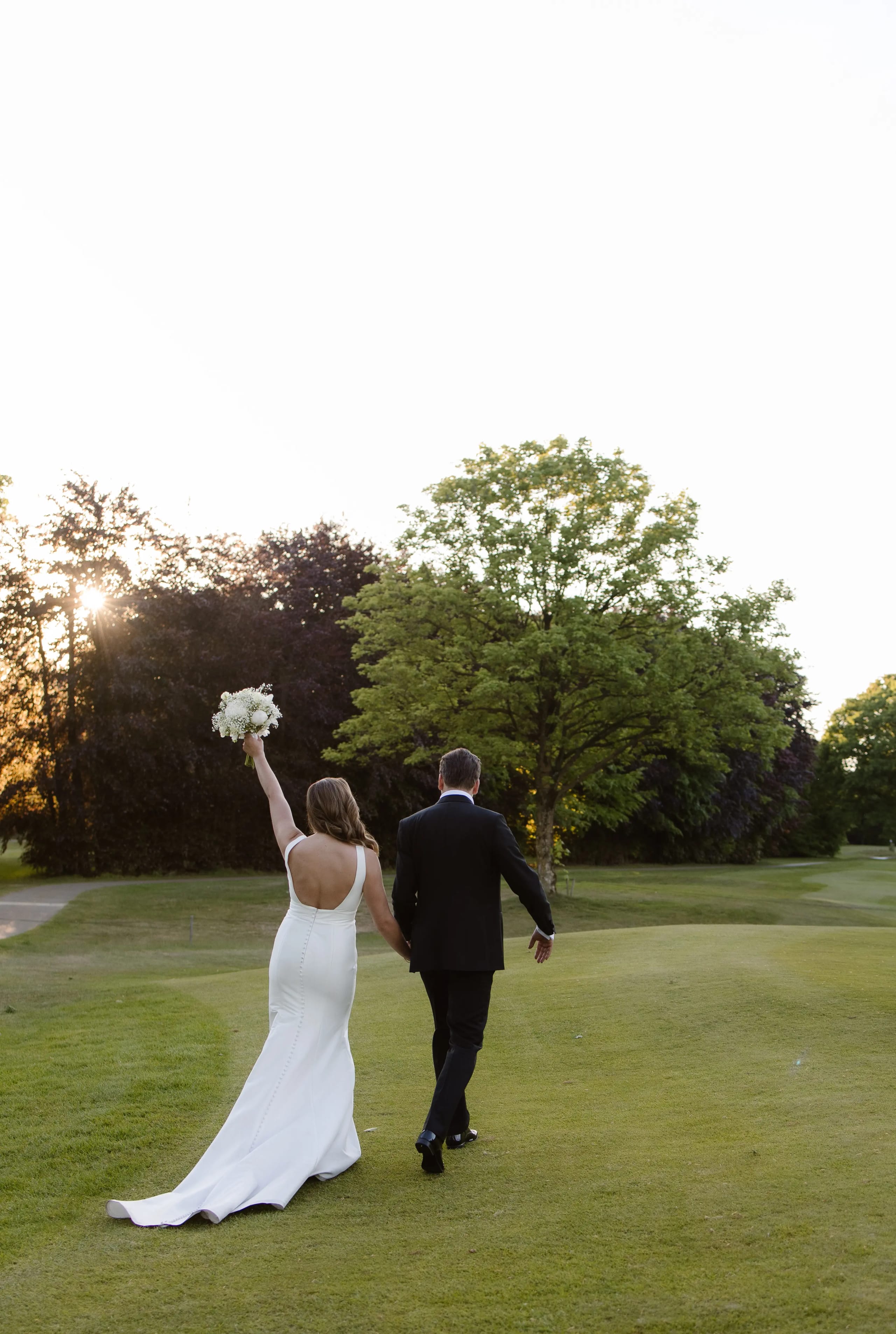 Het bruidspaar wandelt hand in hand over een groen veld tijdens het gouden uur
