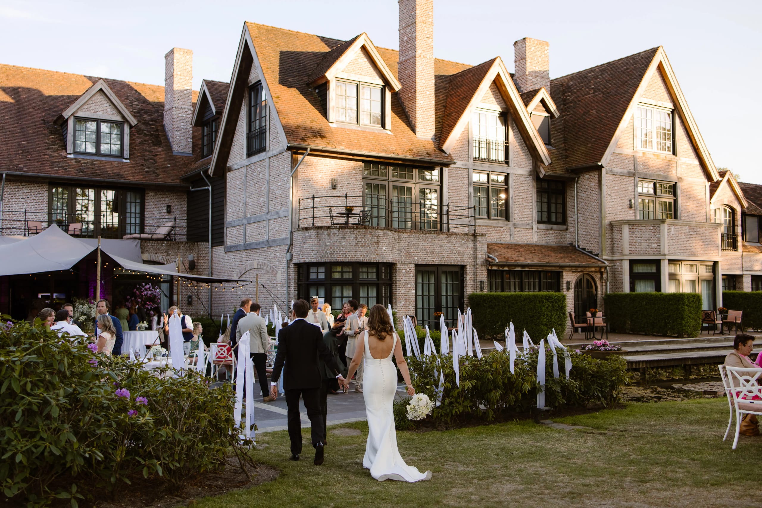 Bruid en bruidegom lopen hand in hand naar een indrukwekkend landhuis
