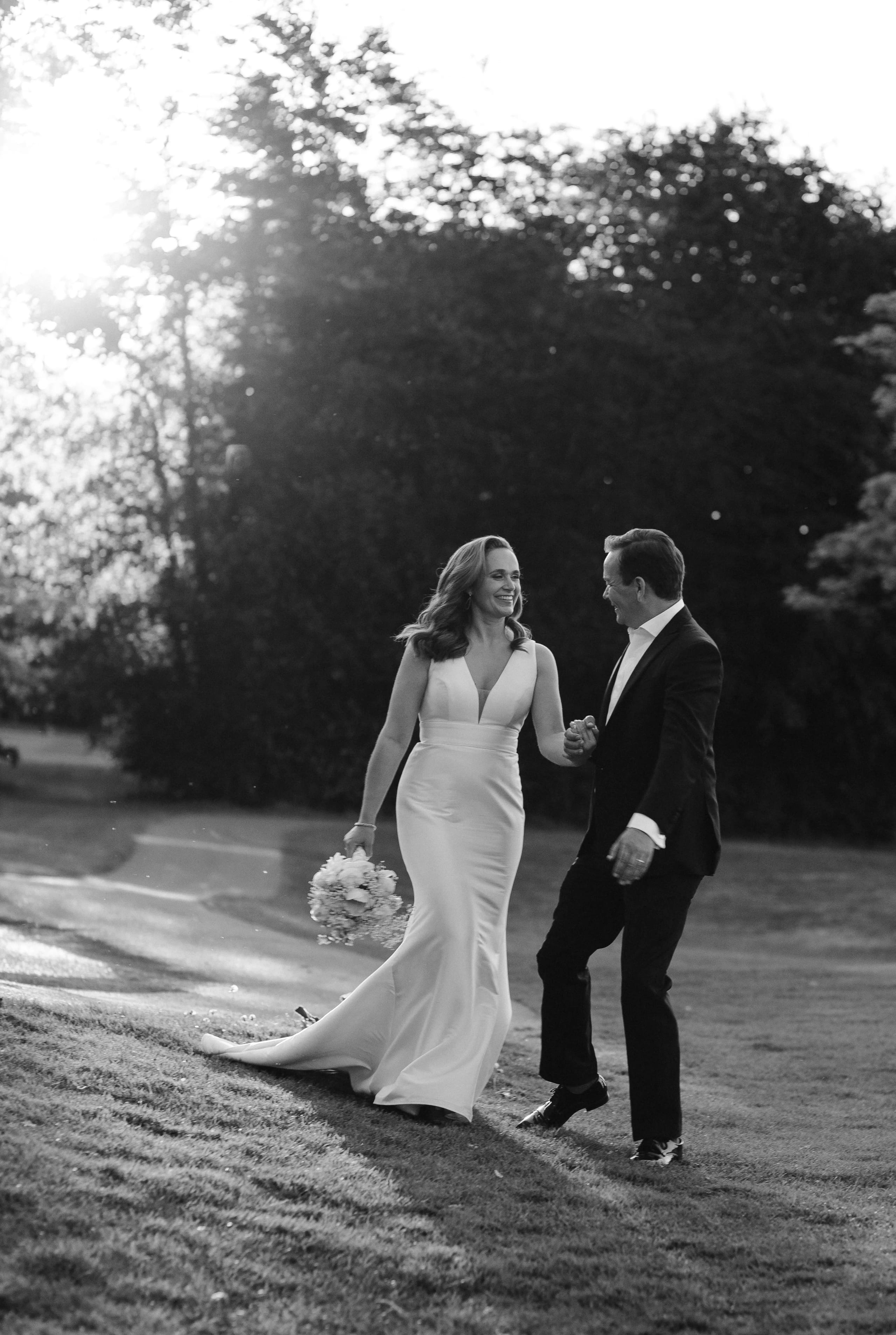 Romantisch zwart-wit portret van het bruidspaar dat samen loopt in een veld bij zonsondergang