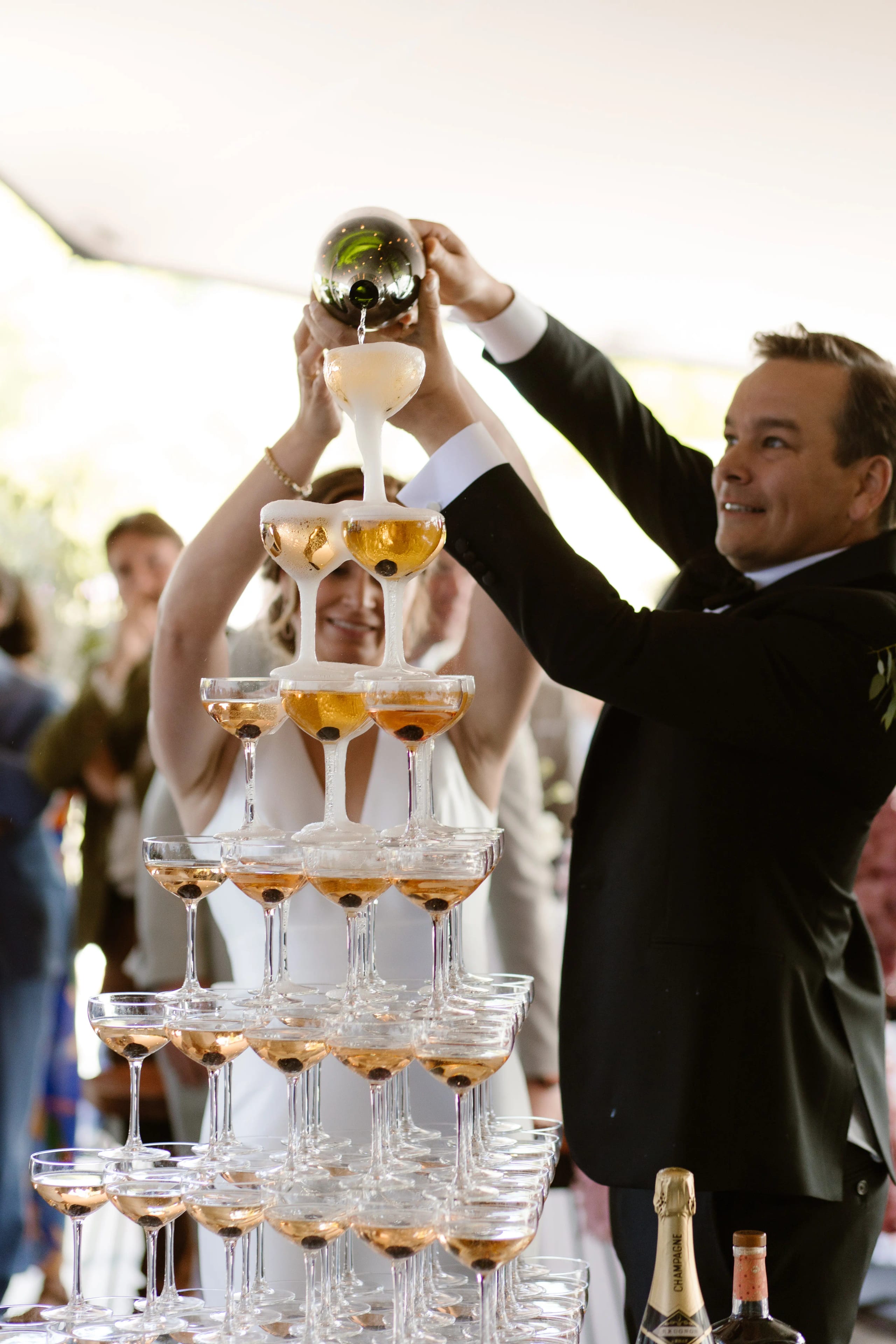 Bruid en bruidegom schenken samen champagne in een grote champagnetoren