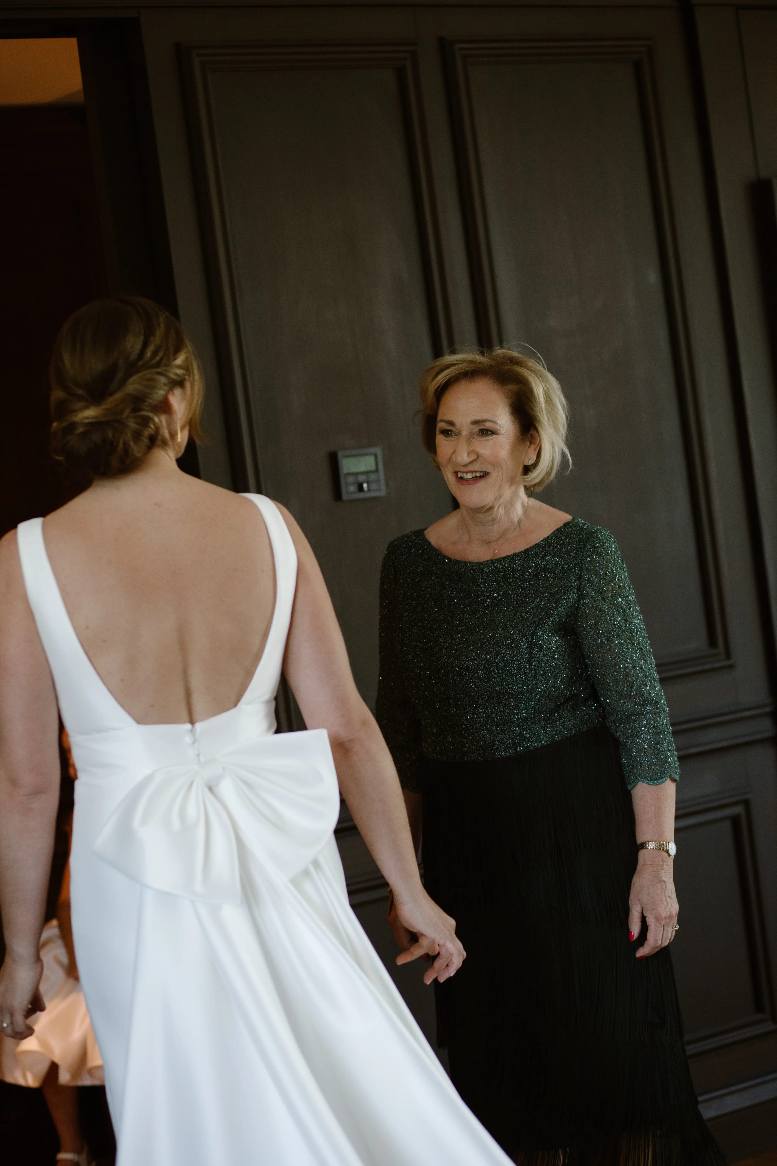 De bruid en haar moeder lachen samen binnenshuis voor een raam