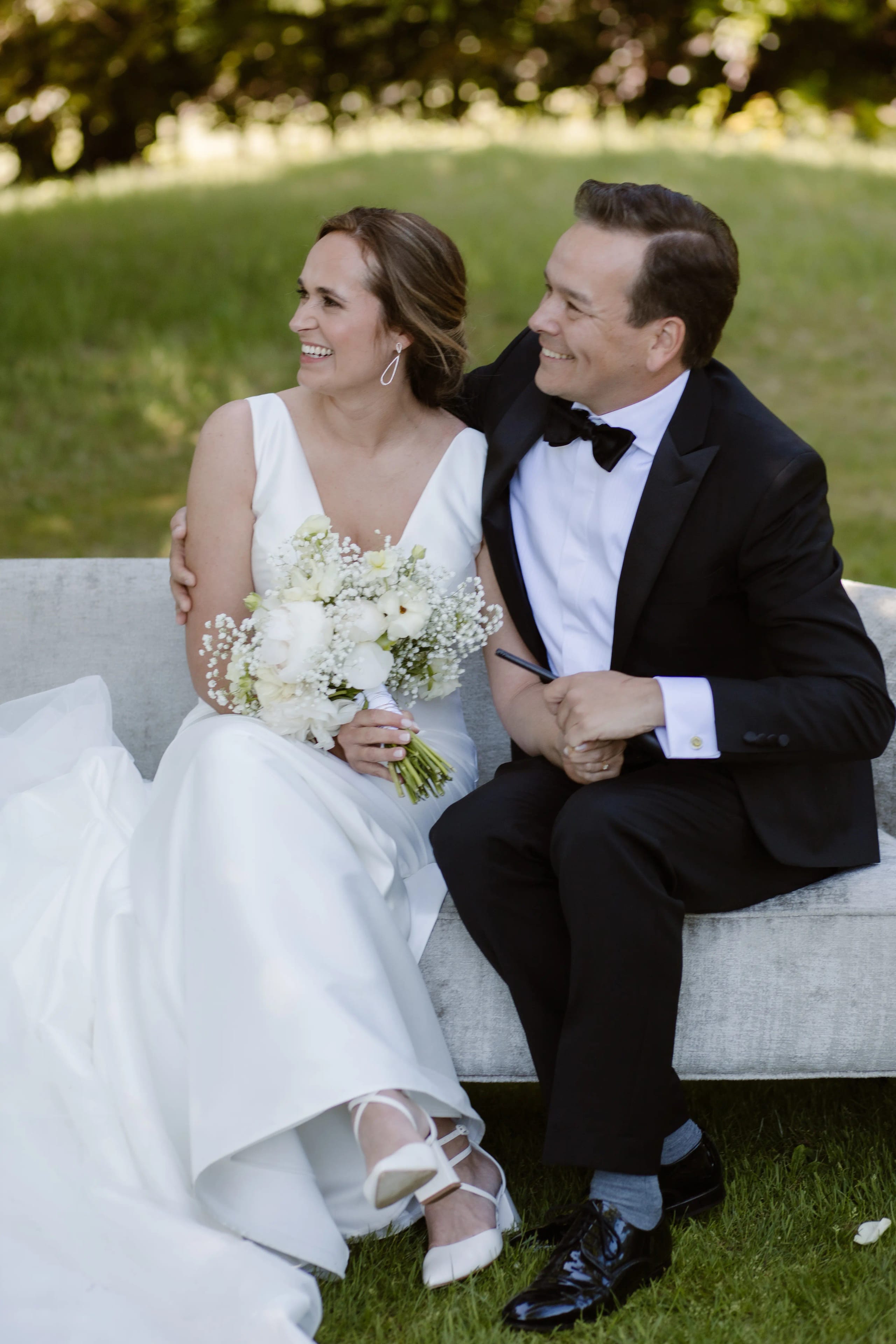 Bruid en bruidegom zitten samen op een bankje in het park en kijken elkaar lachend aan