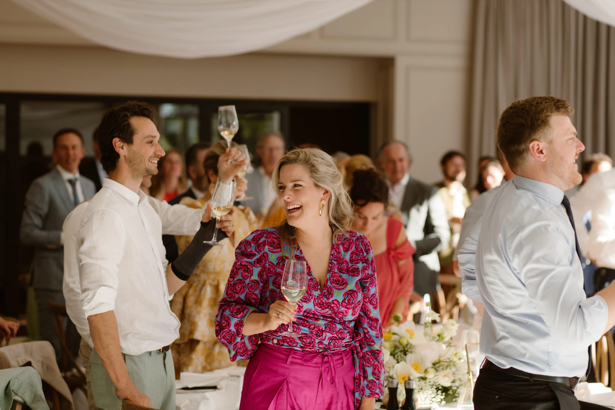 Een gast in een fleurige roze blouse lacht tijdens de bruiloft