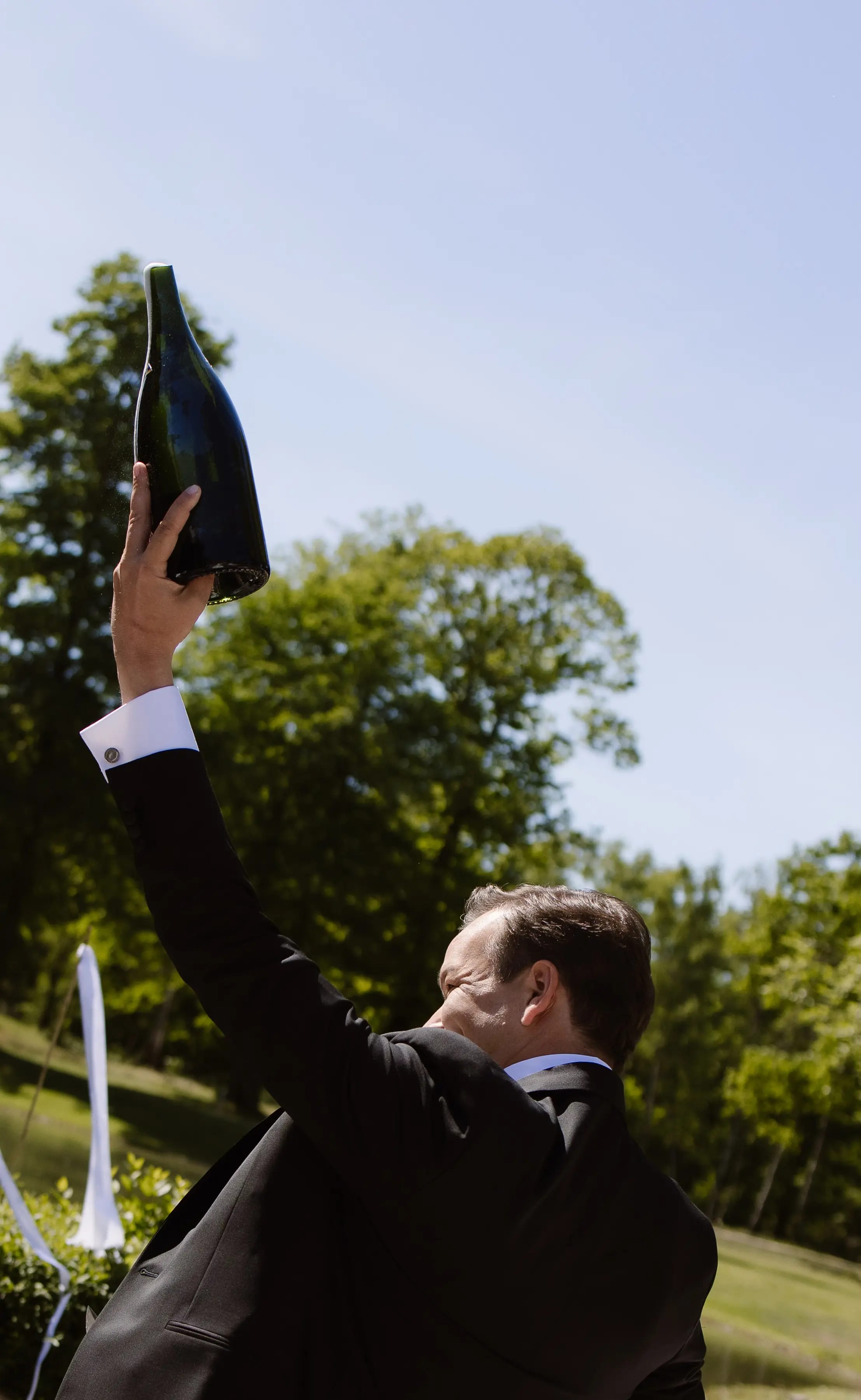 De bruidegom houdt een grote fles champagne triomfantelijk in de lucht