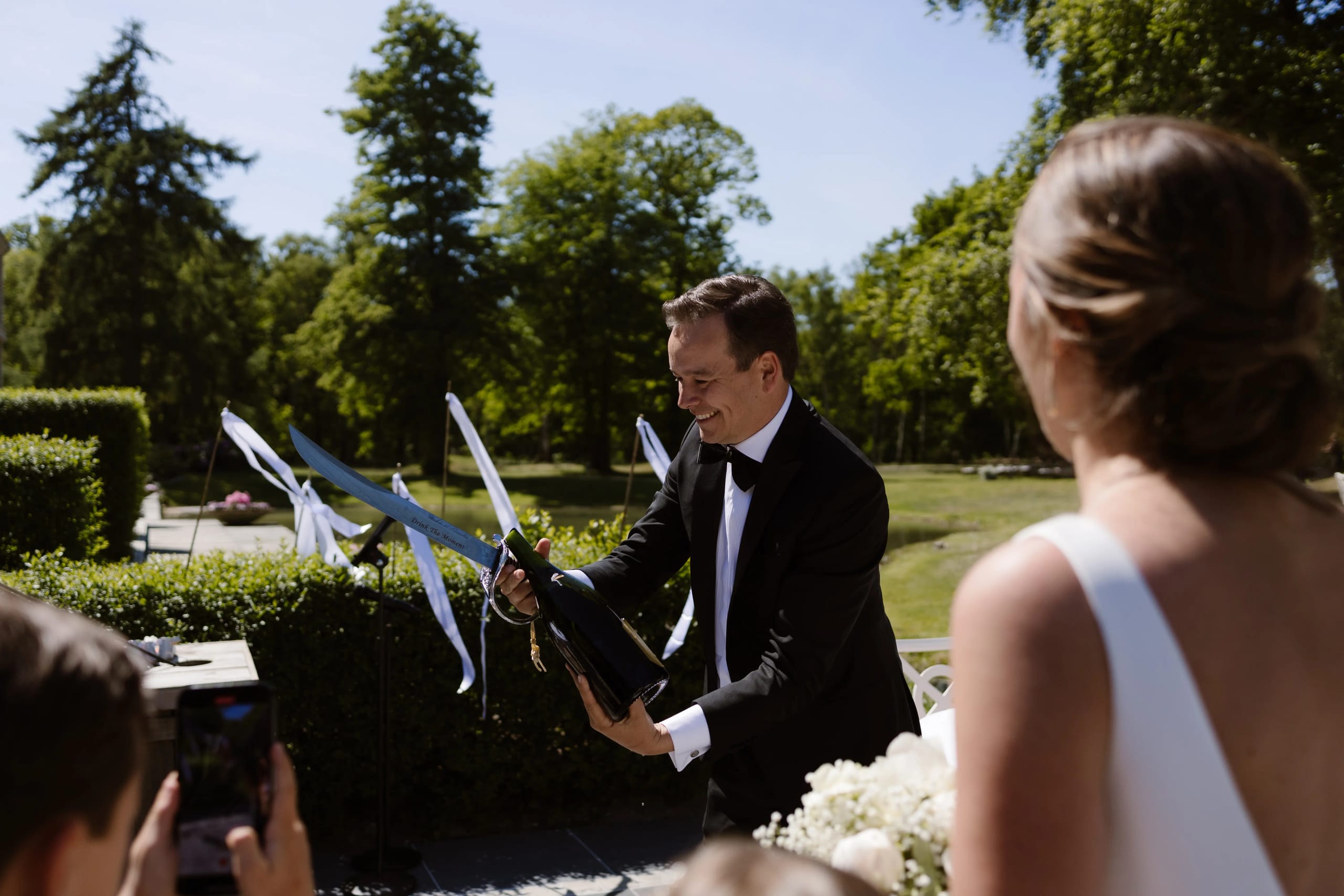 De bruidegom ontkurkt enthousiast een fles champagne met een sabel