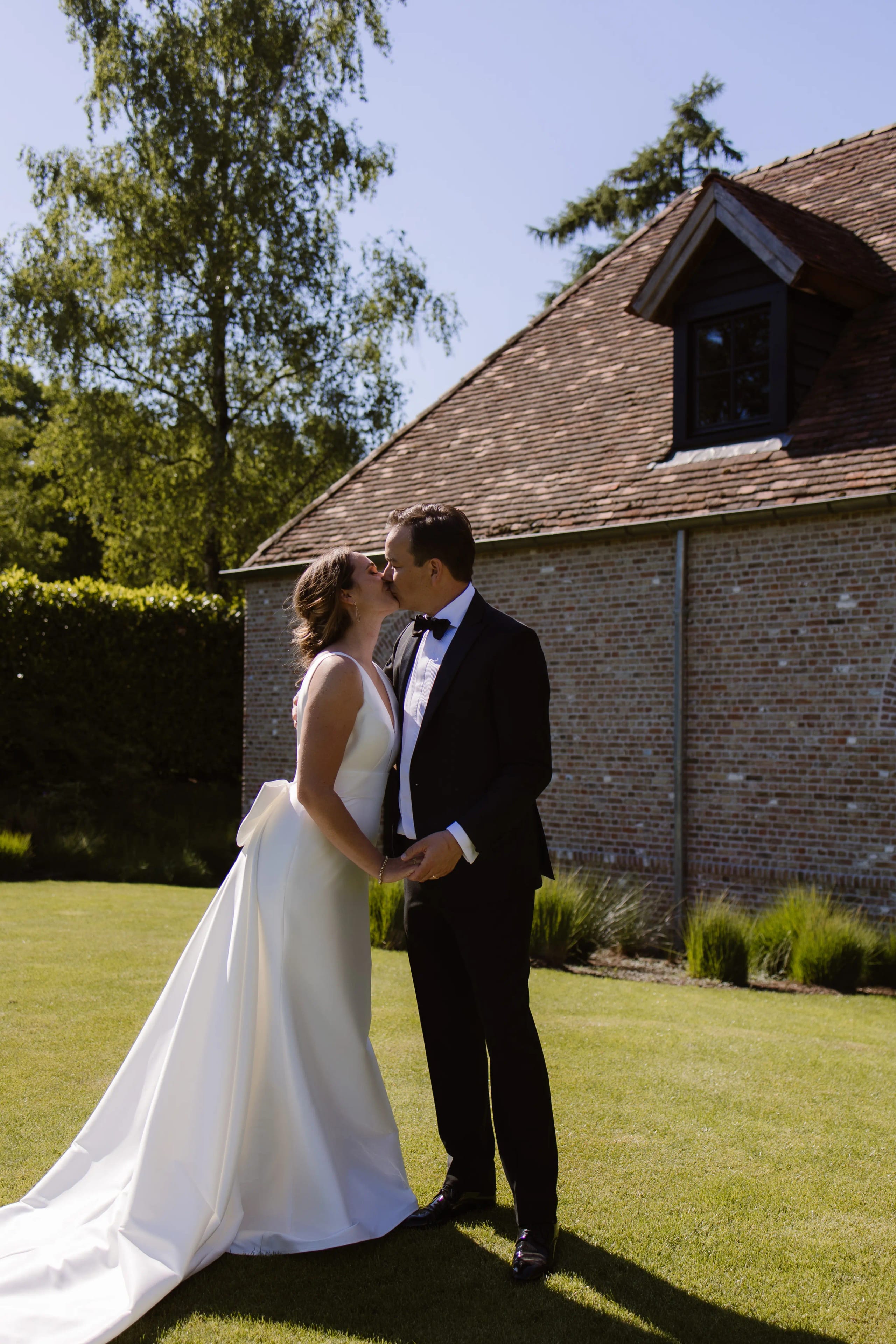 Het bruidspaar geeft elkaar een kus in de zon voor een stenen gebouw