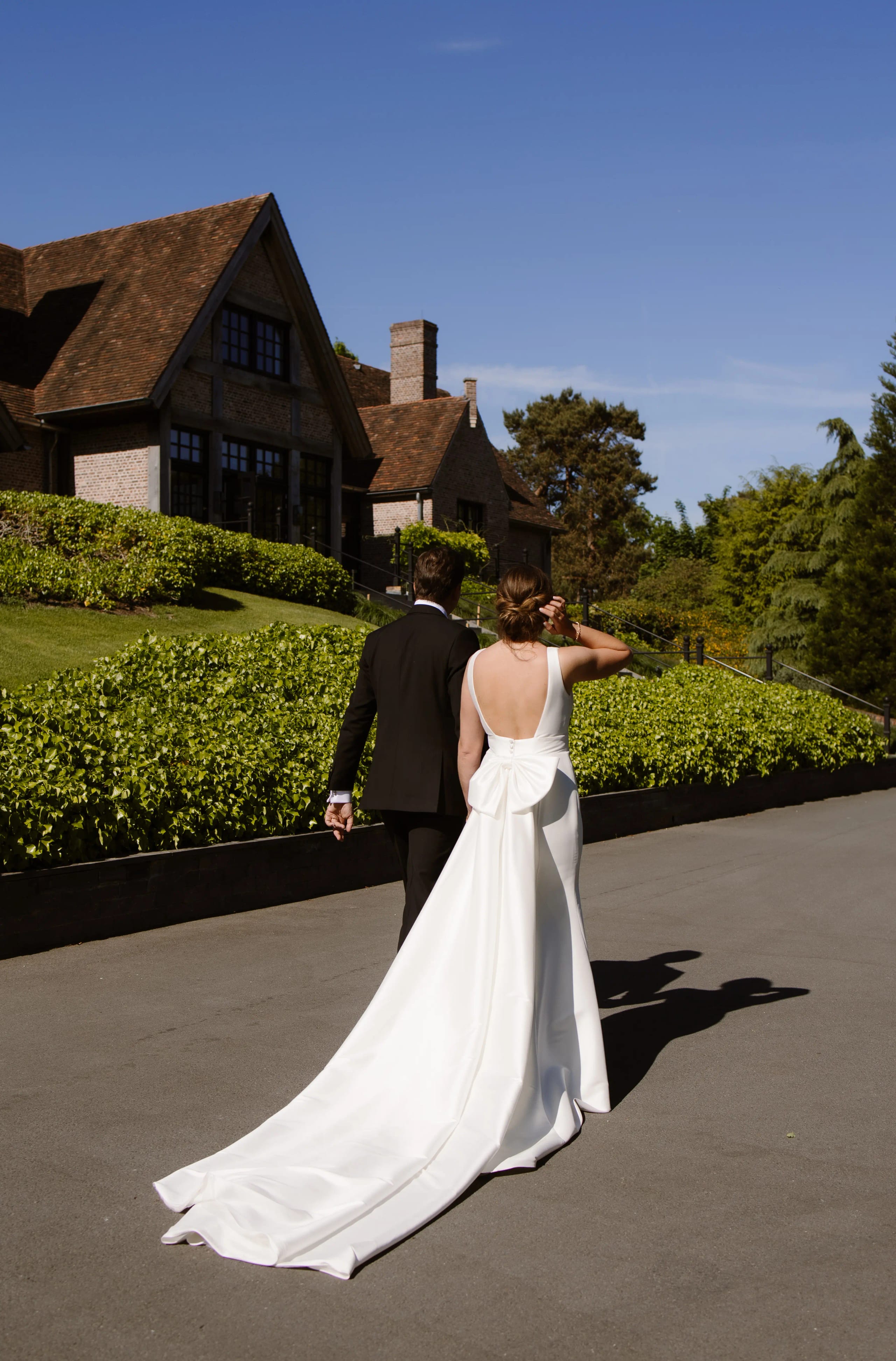 De bruid en bruidegom lopen weg bij het landhuis, de lange sleep van de jurk is goed zichtbaar