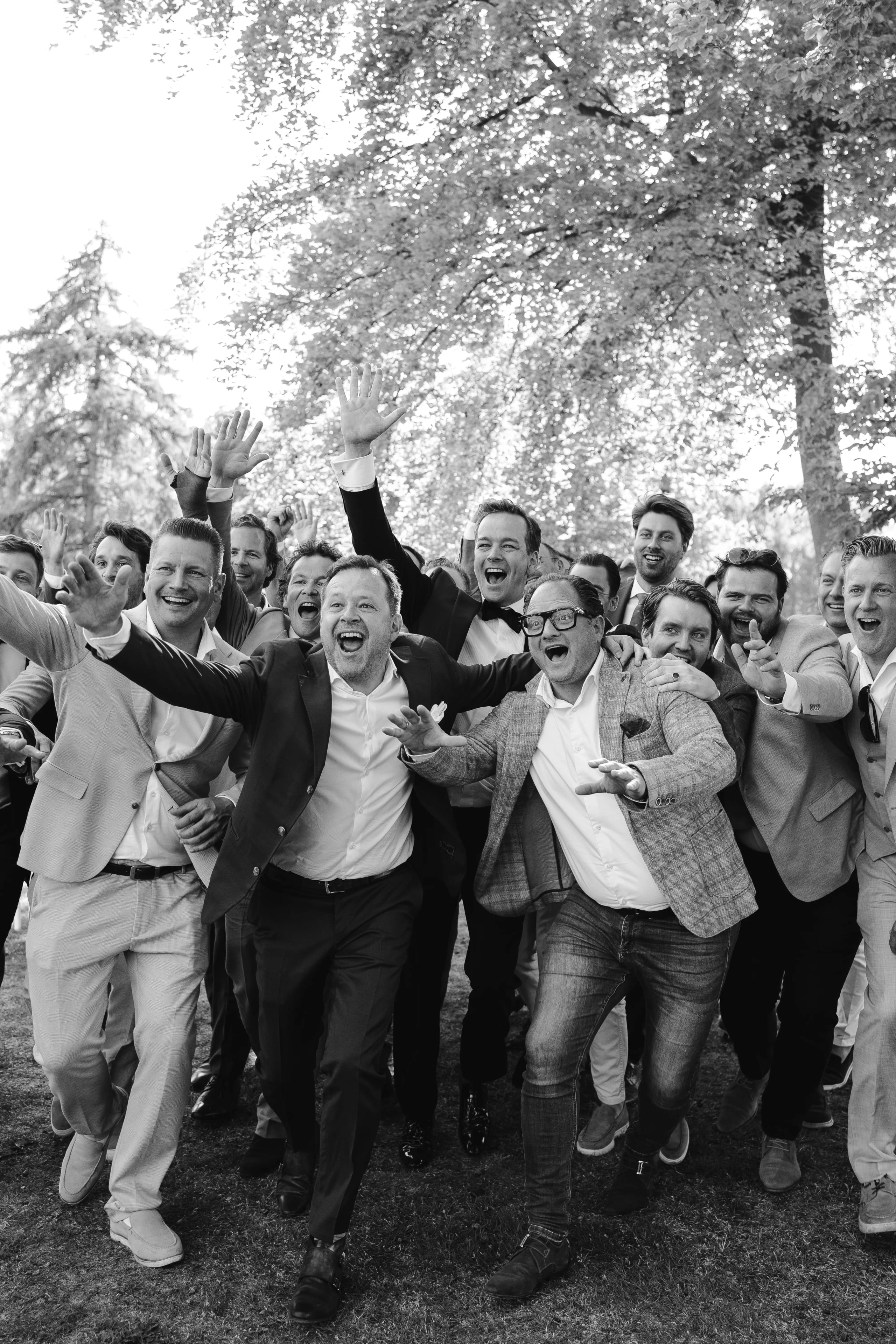 Vrolijke zwart-wit foto van de bruidegom en zijn vrienden die juichend de armen in de lucht steken