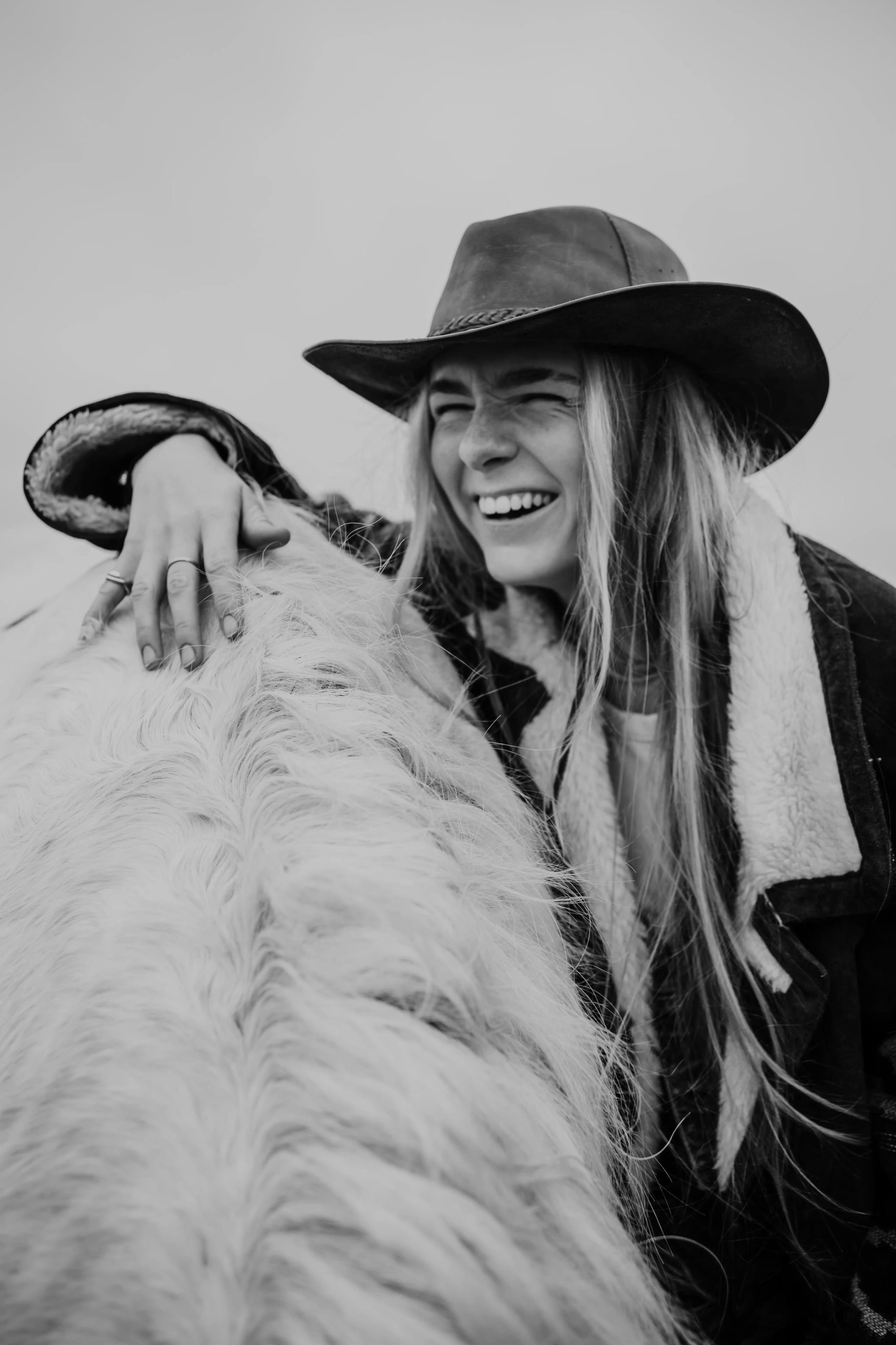 Lachende Lies Zhara knuffelt met een wit paard, zwart-wit fotografie