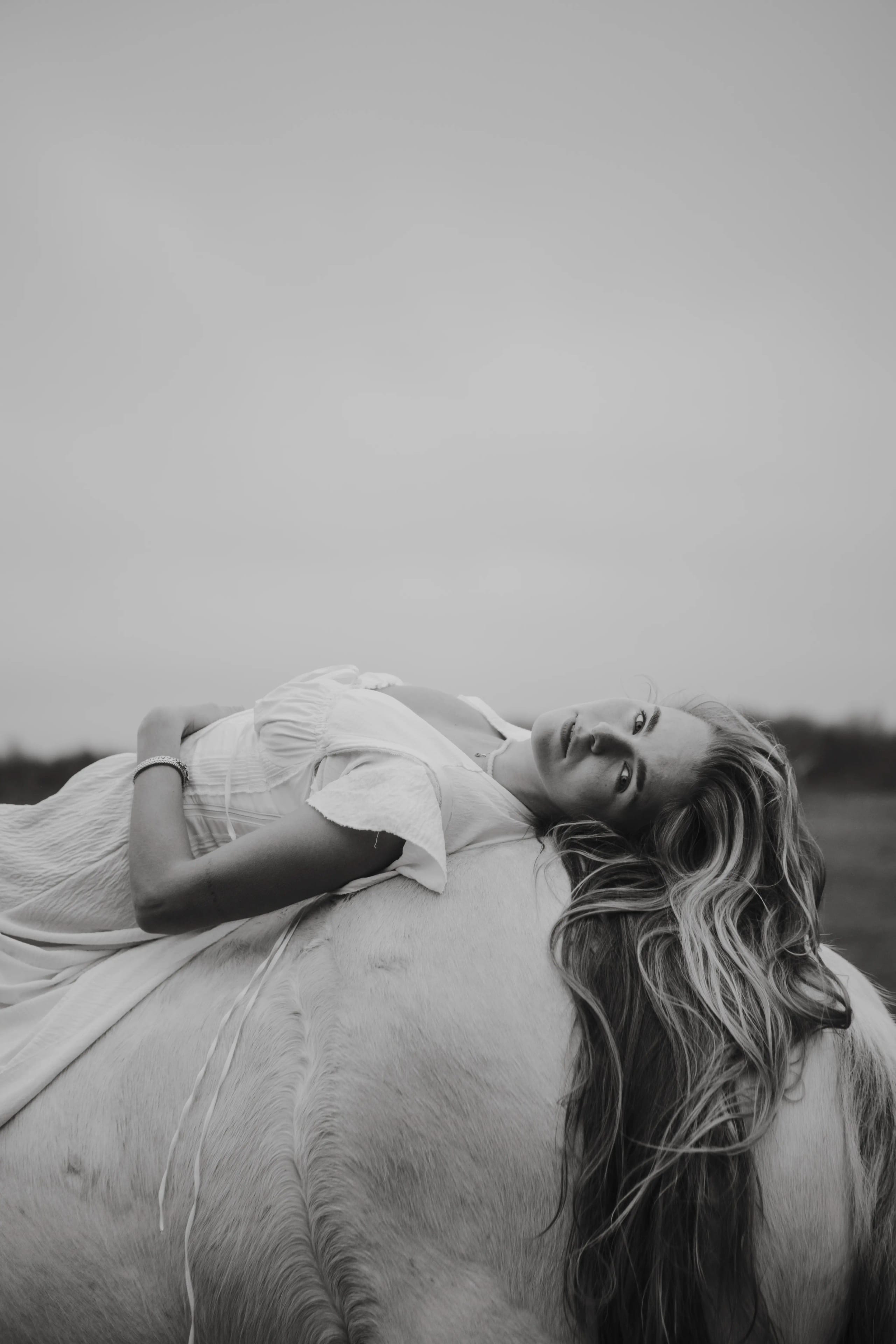 Lies Zhara liggend op de rug van een wit paard, artistiek portret