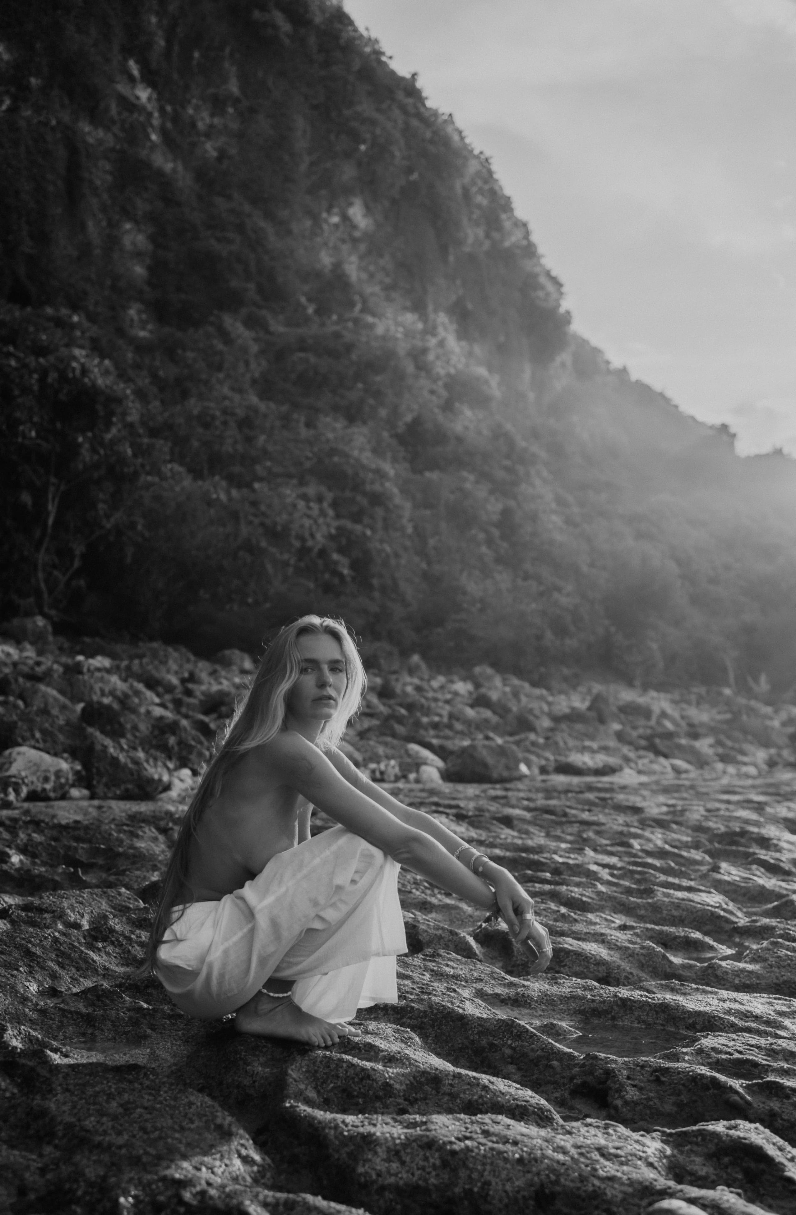 Lies Zhara zittend op een rotsachtig strand in Bali, zwart-wit