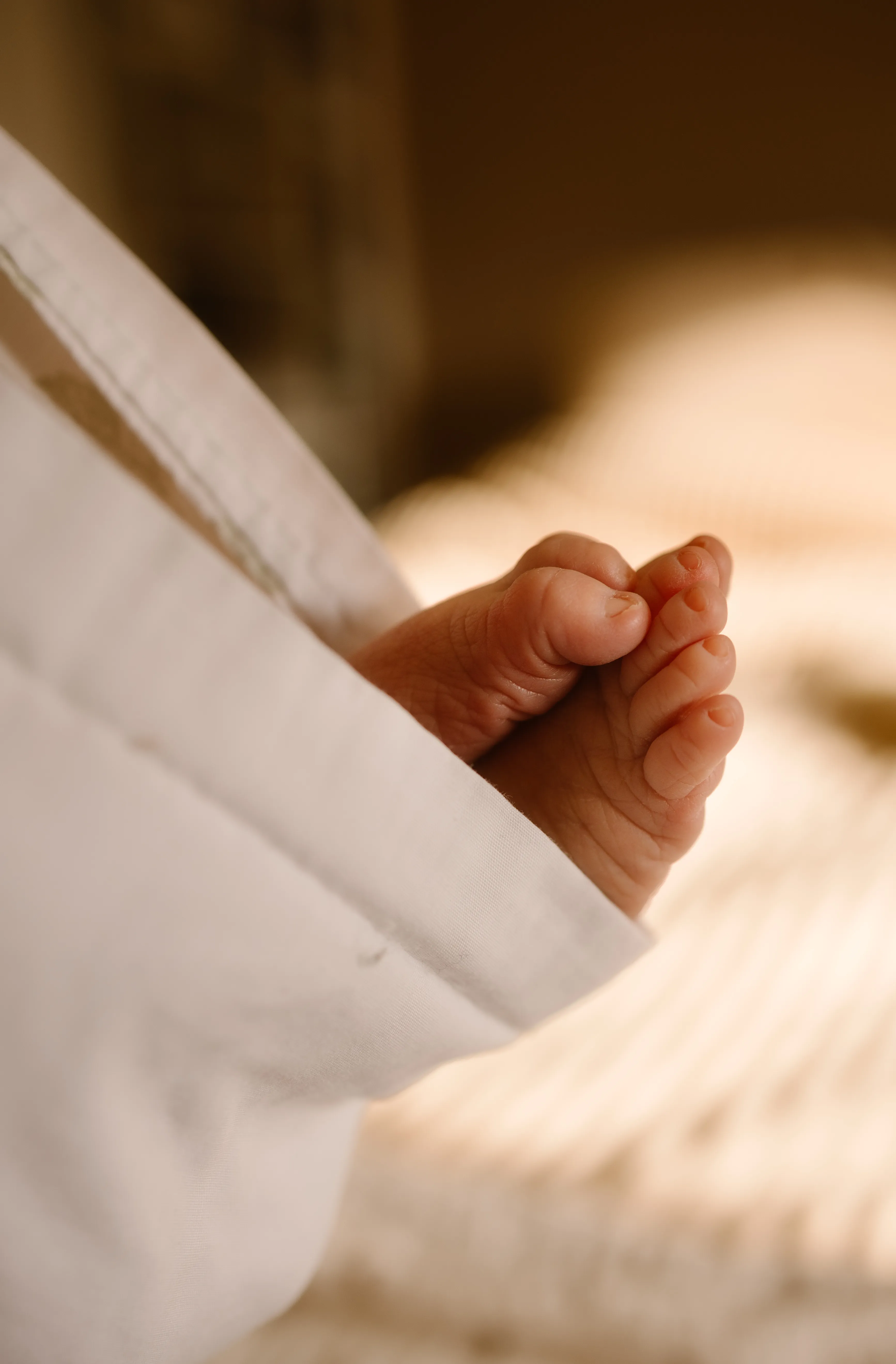 Een close-up van de kleine voetjes van een baby die voorzichtig uit een witte deken steken, met een warme en serene achtergrond.