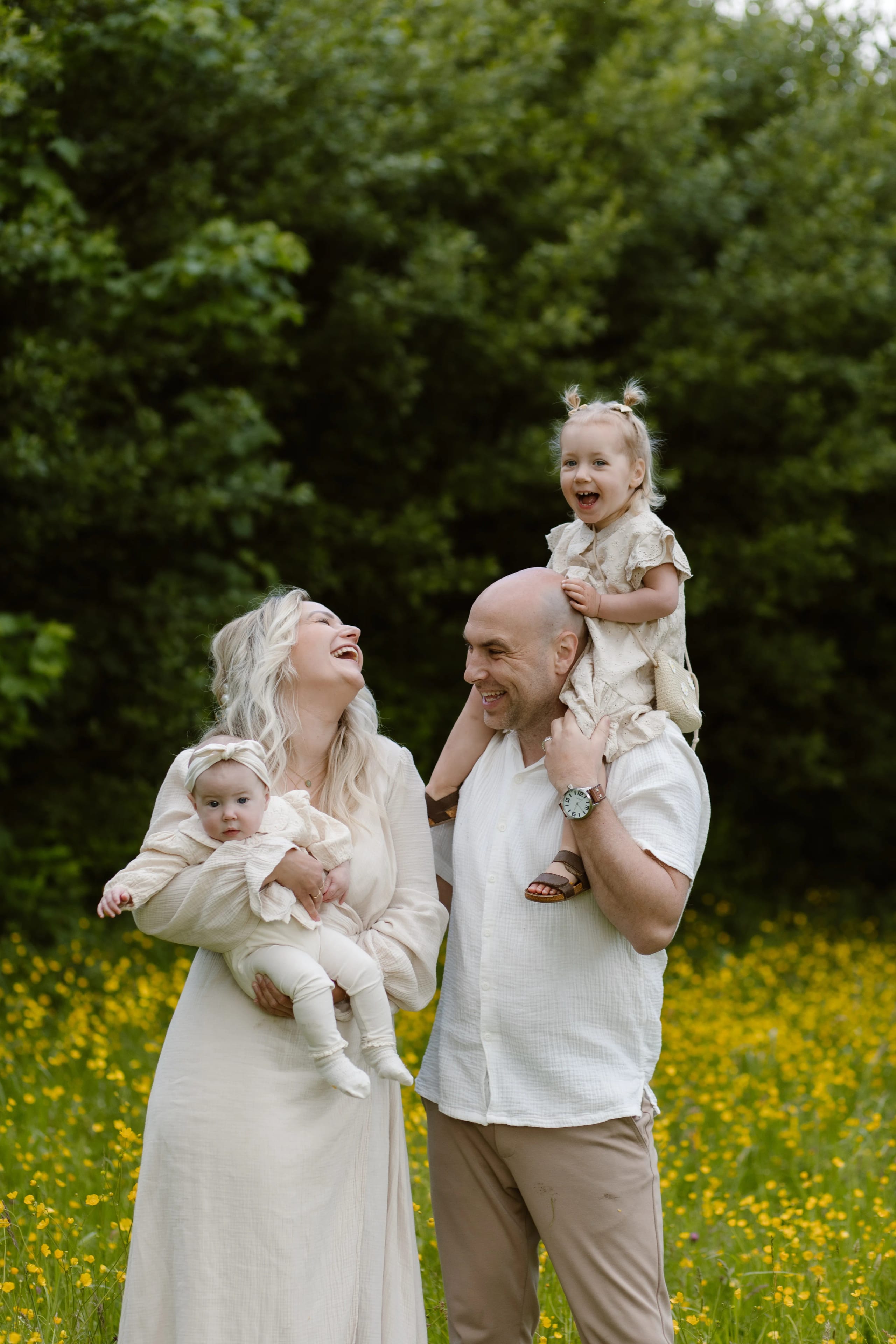 Een gelukkige familie staat in een bloeiend veld met gele bloemen, de moeder met een baby in haar armen and the father met hun peuter op zijn schouders, terwijl ze samen lachen en genieten van het moment.