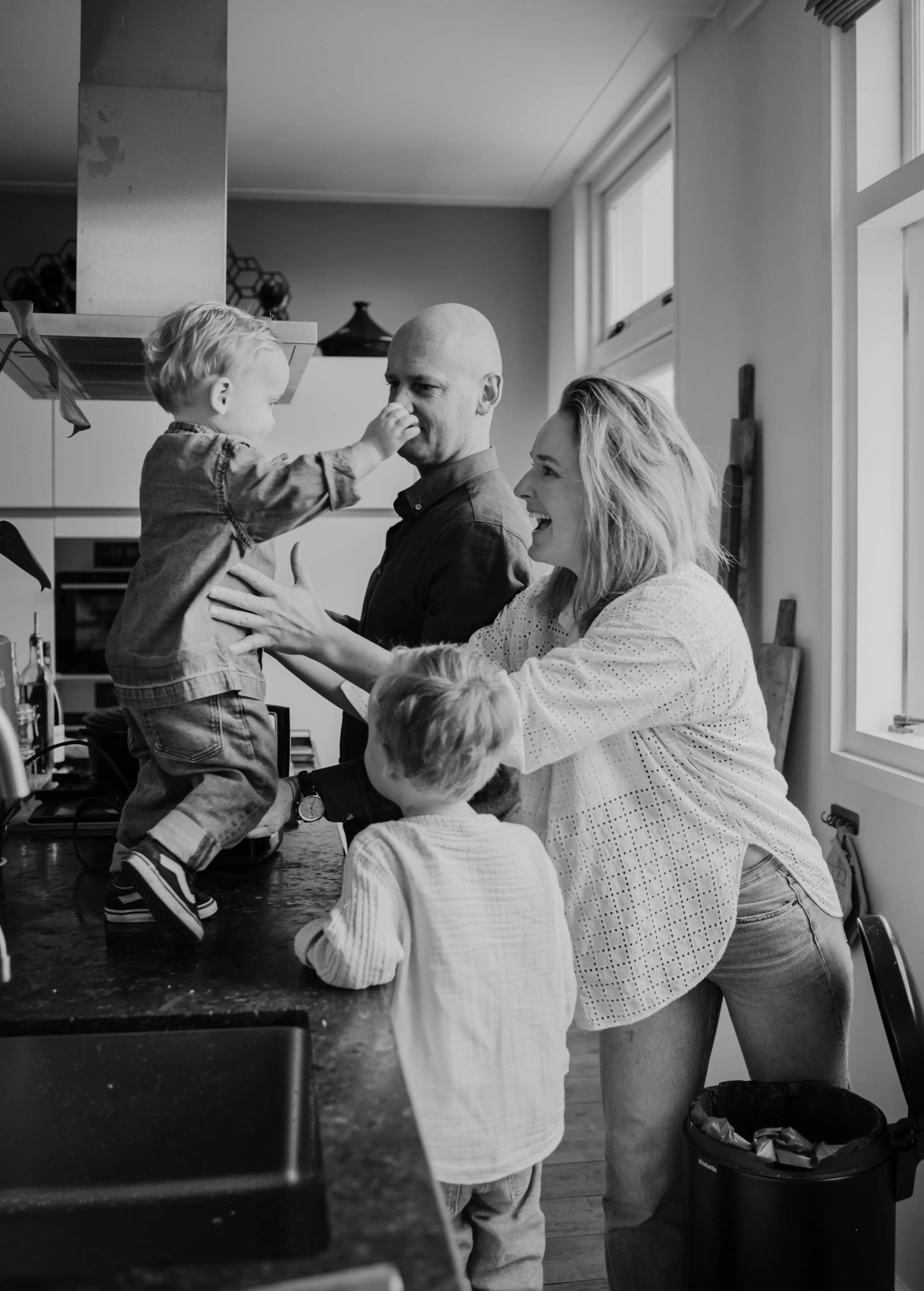 Zwart-wit foto van een vrolijk gezin in de keuken, spontane familiefotografie aan huis.